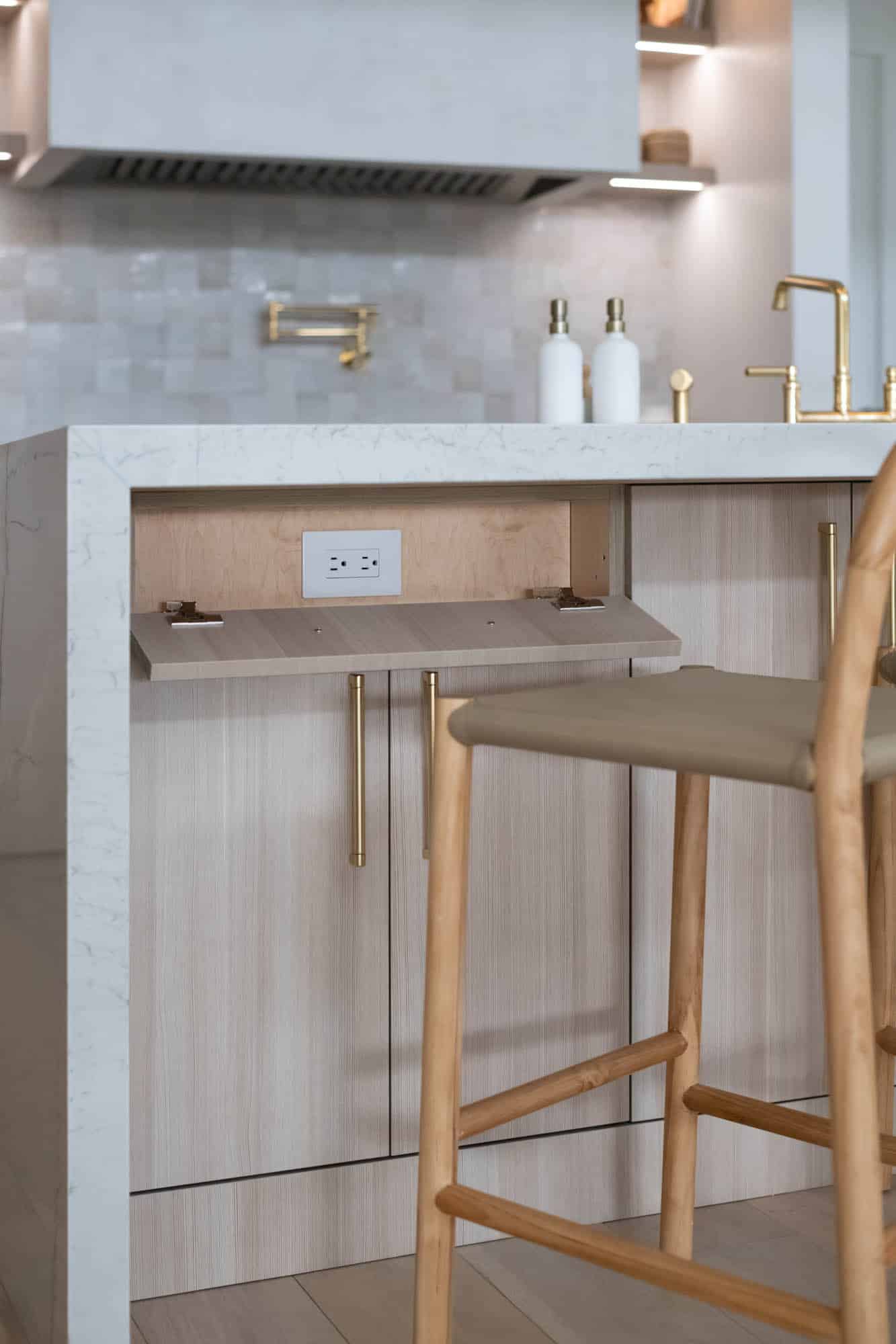 Luxury kitchen island with hidden pop-out outlets, marble waterfall countertop, brass fixtures, and light wood cabinetry in a Centennial Hills Las Vegas remodel by Kingdom & Co.