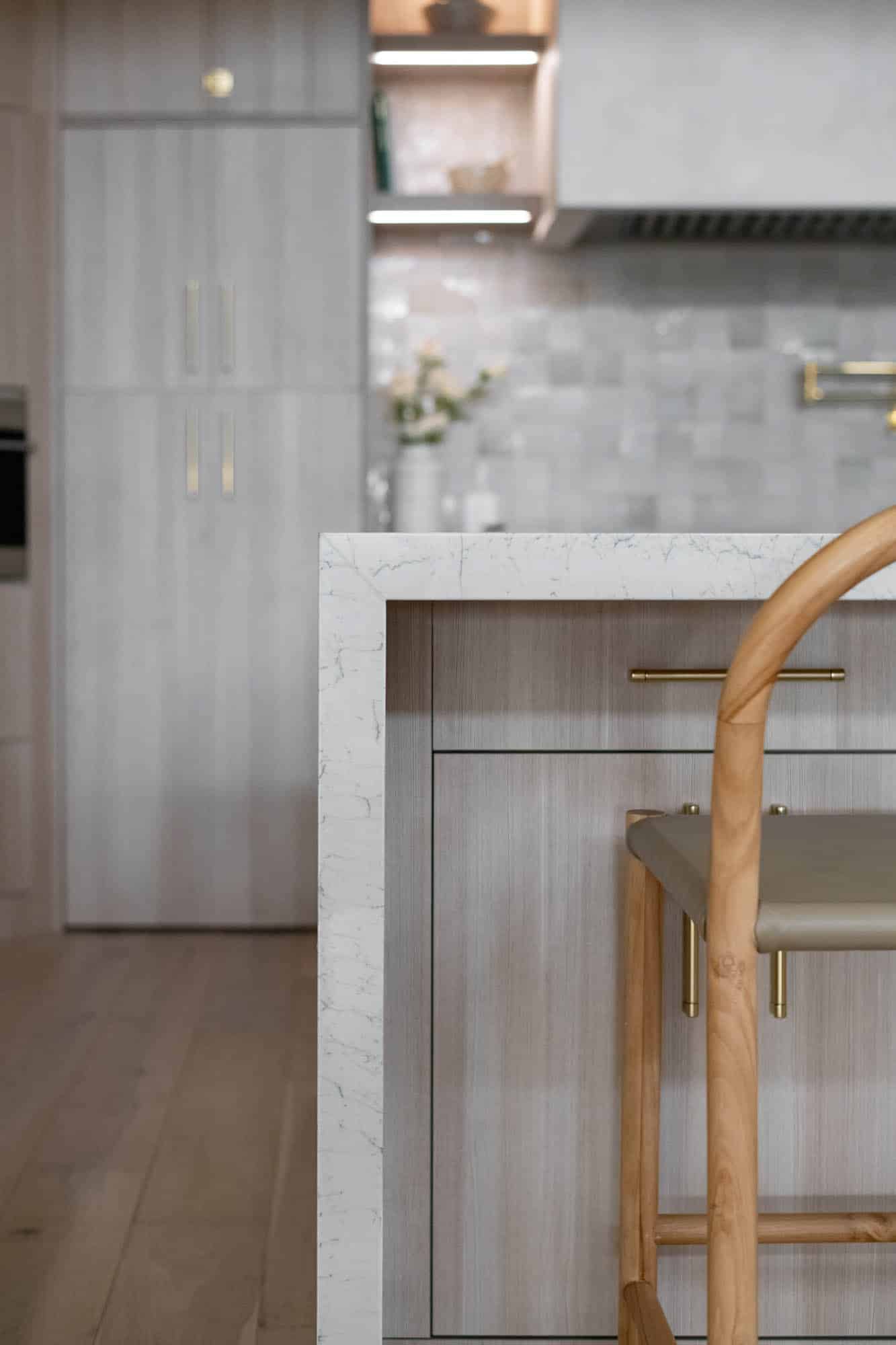 Luxury kitchen remodel in Centennial Hills Las Vegas featuring a waterfall marble island, light wood cabinetry, brass hardware, and modern tile backsplash by Kingdom & Co.