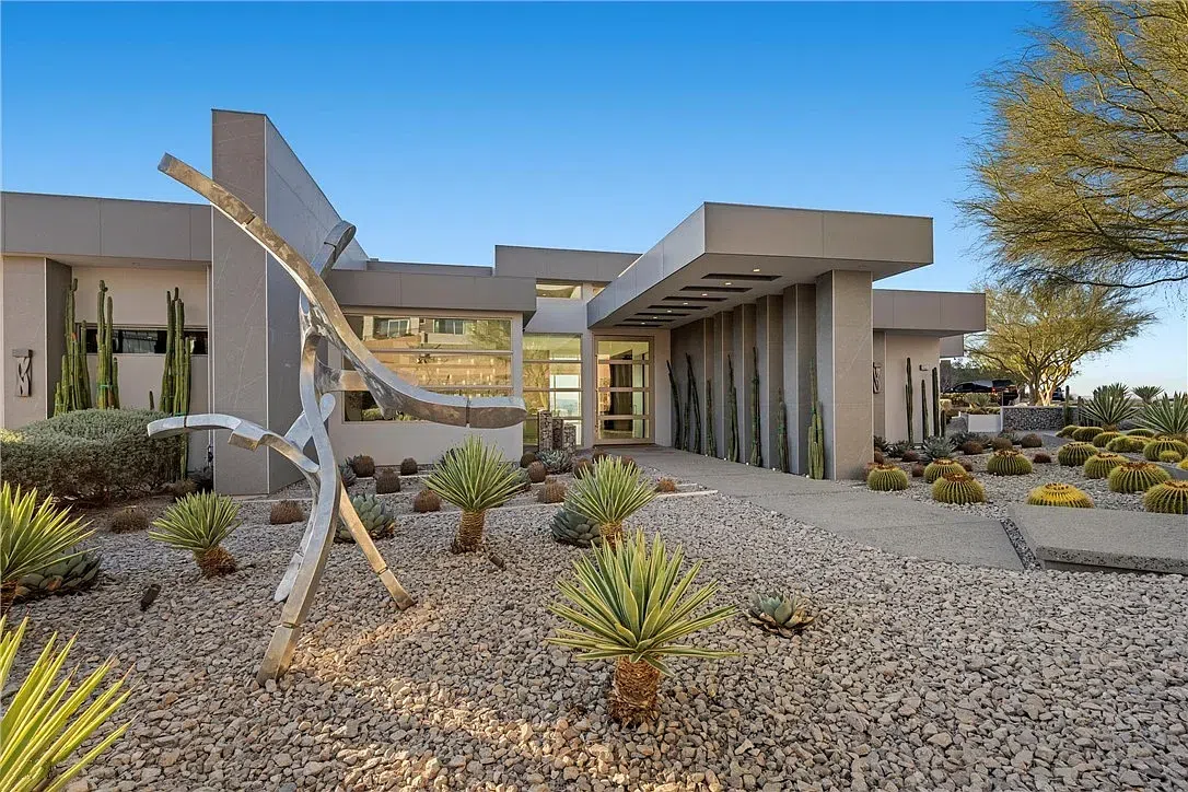 Custom desert-smart luxury home with white and wood façade, large windows, deep overhangs, and desert landscaping — perfectly aligned to minimize heat gain