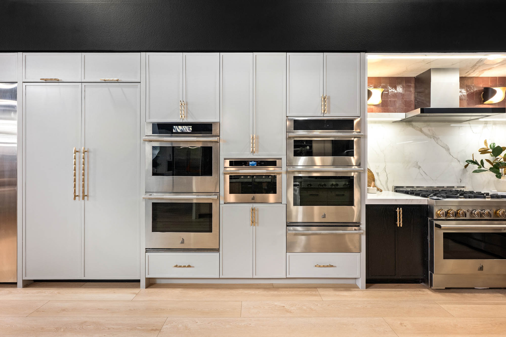 FergusonShowroom_CommercialRemodel_Kingdomandco Wall of built-in stainless ovens and white cabinetry with brass hardware designed by Kingdom & Co.