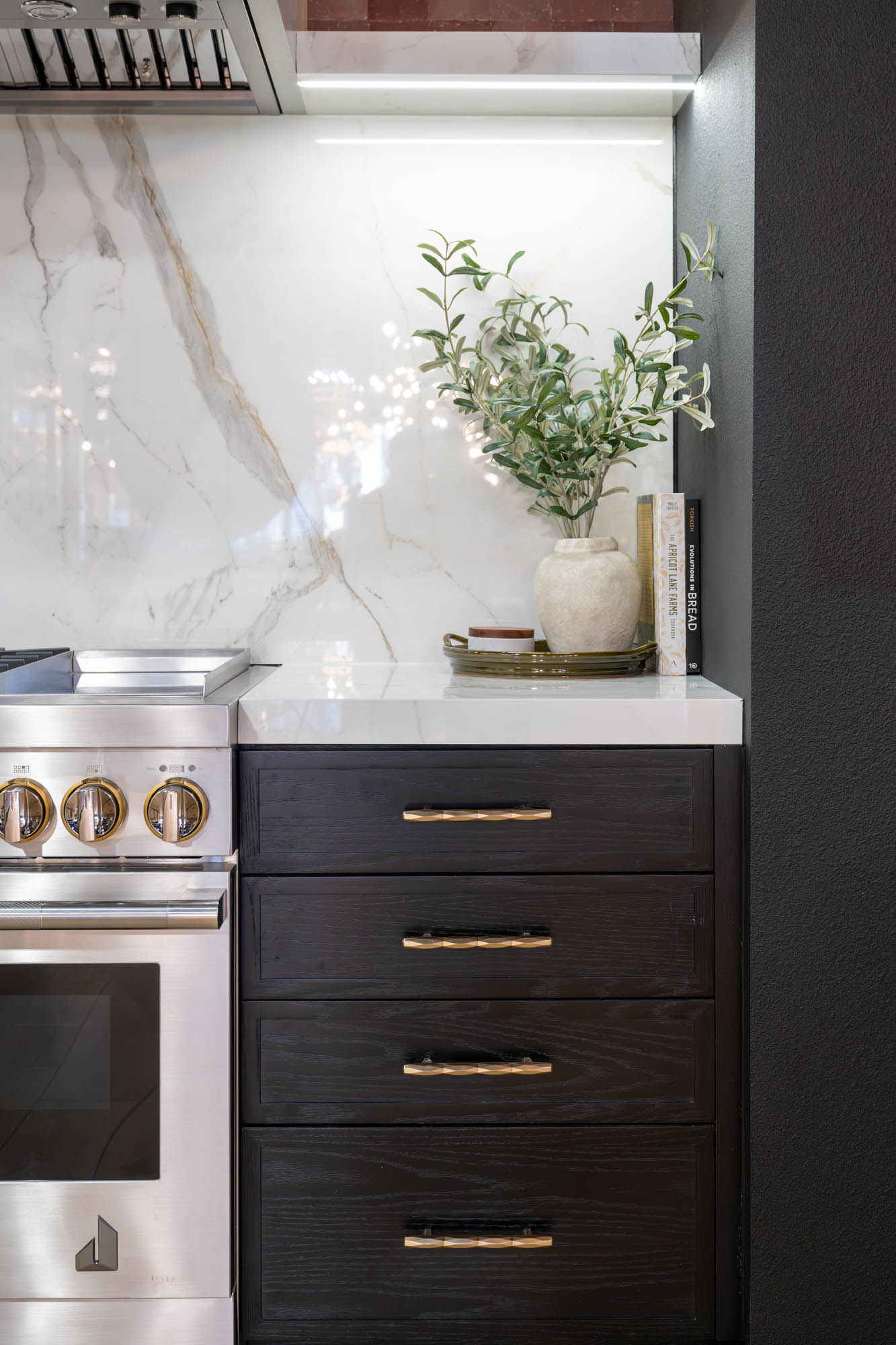 Close-up of marble backsplash and stainless steel range with brass accents designed by Kingdom & Co Las Vegas.