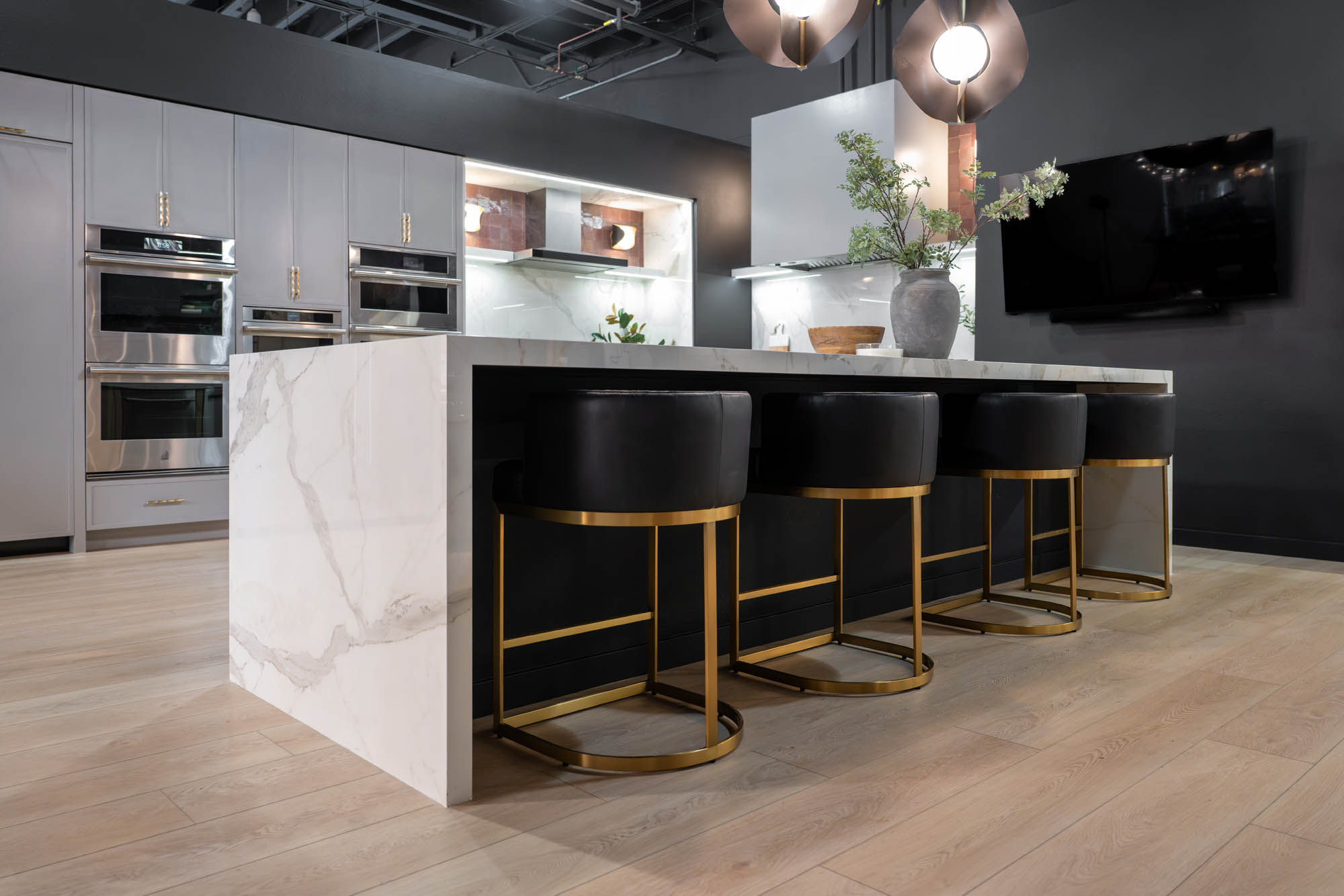 Marble waterfall island with black and brass barstools in contemporary kitchen designed by Kingdom & Co.