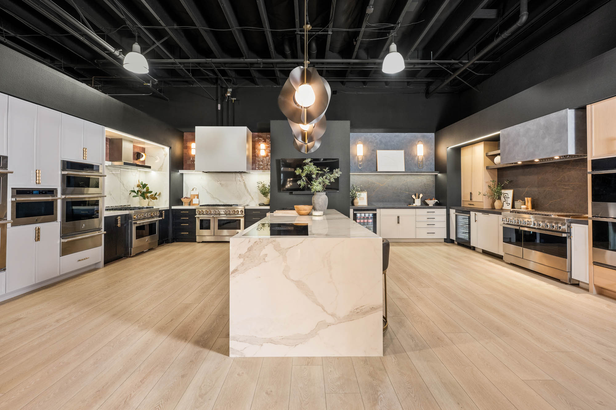FergusonShowroom_CommercialRemodel_Kingdomandco Modern showroom kitchen with marble waterfall island, dark ceilings, and brass lighting designed by Kingdom & Co Las Vegas.