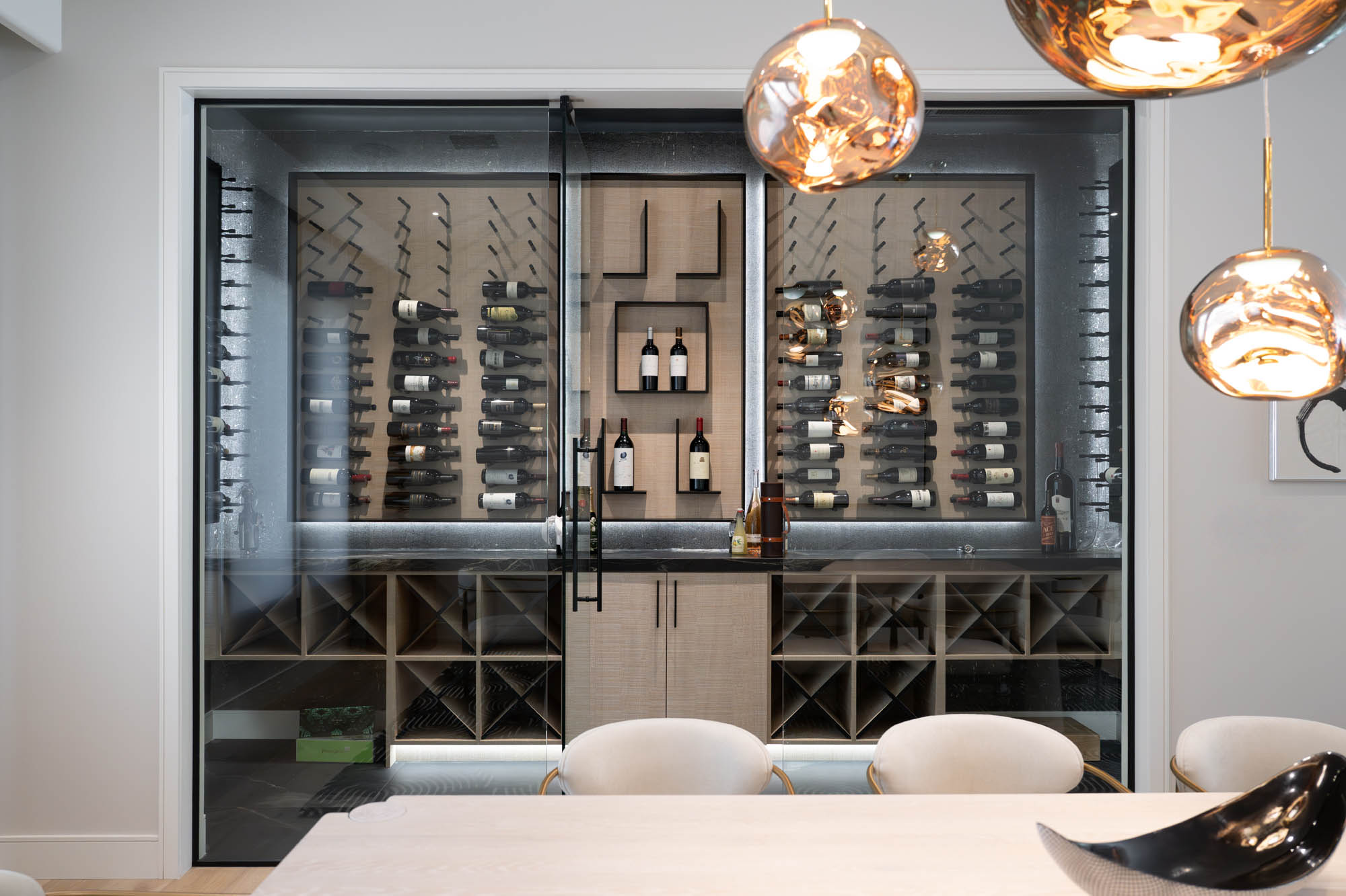 The Lucida_summerlin-south_luxury-remodel_kingdomandco Dining room with illuminated glass wine cellar and modern lighting, remodeled by Kingdom & Co in Summerlin South.