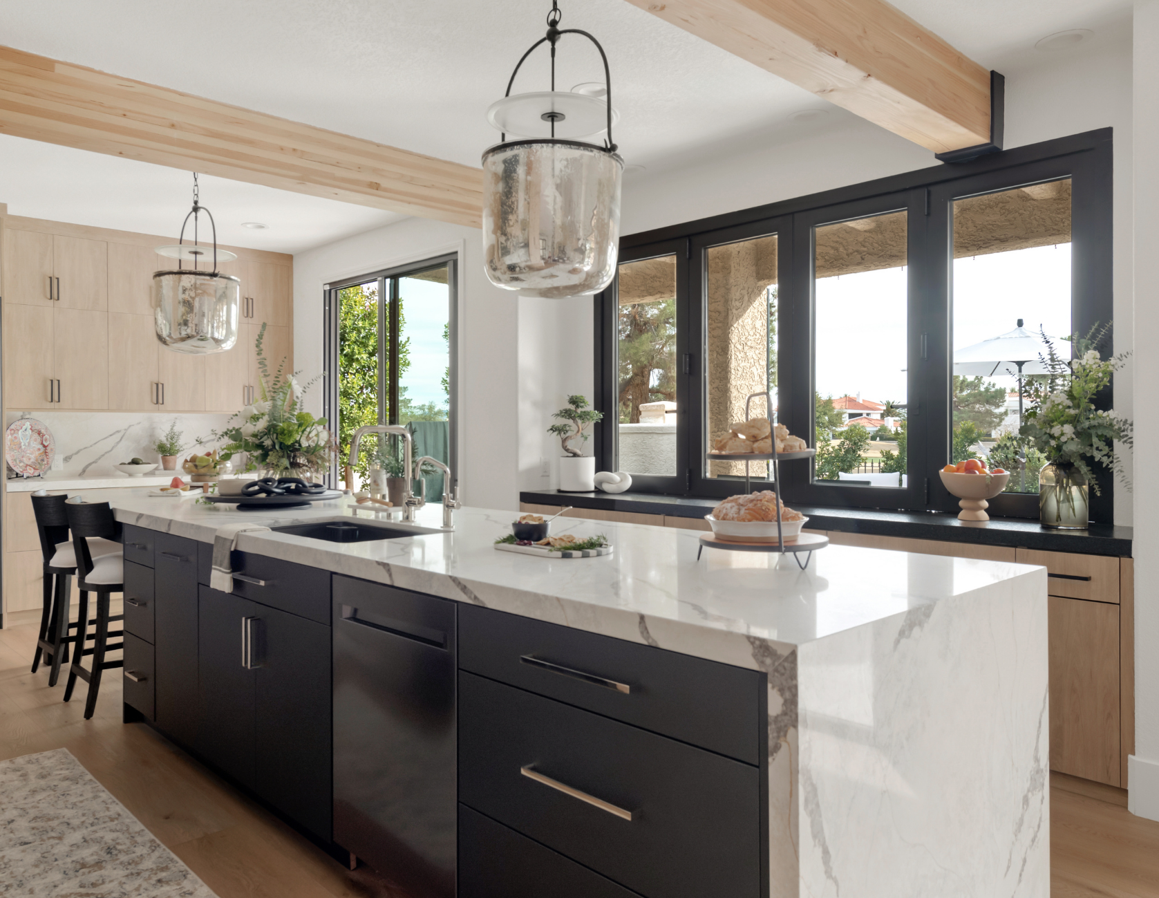 After: Light wood cabinetry with marble countertops, glass pendant lights, and exposed wood beam in The Parker kitchen remodel