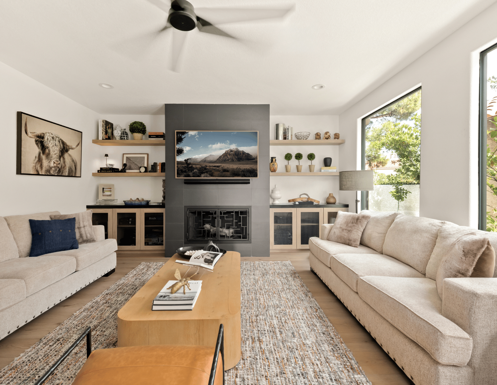 After: Contemporary living room with cream sofas, natural wood coffee table, and built-in shelving around TV in The Parker Las Vegas remodel