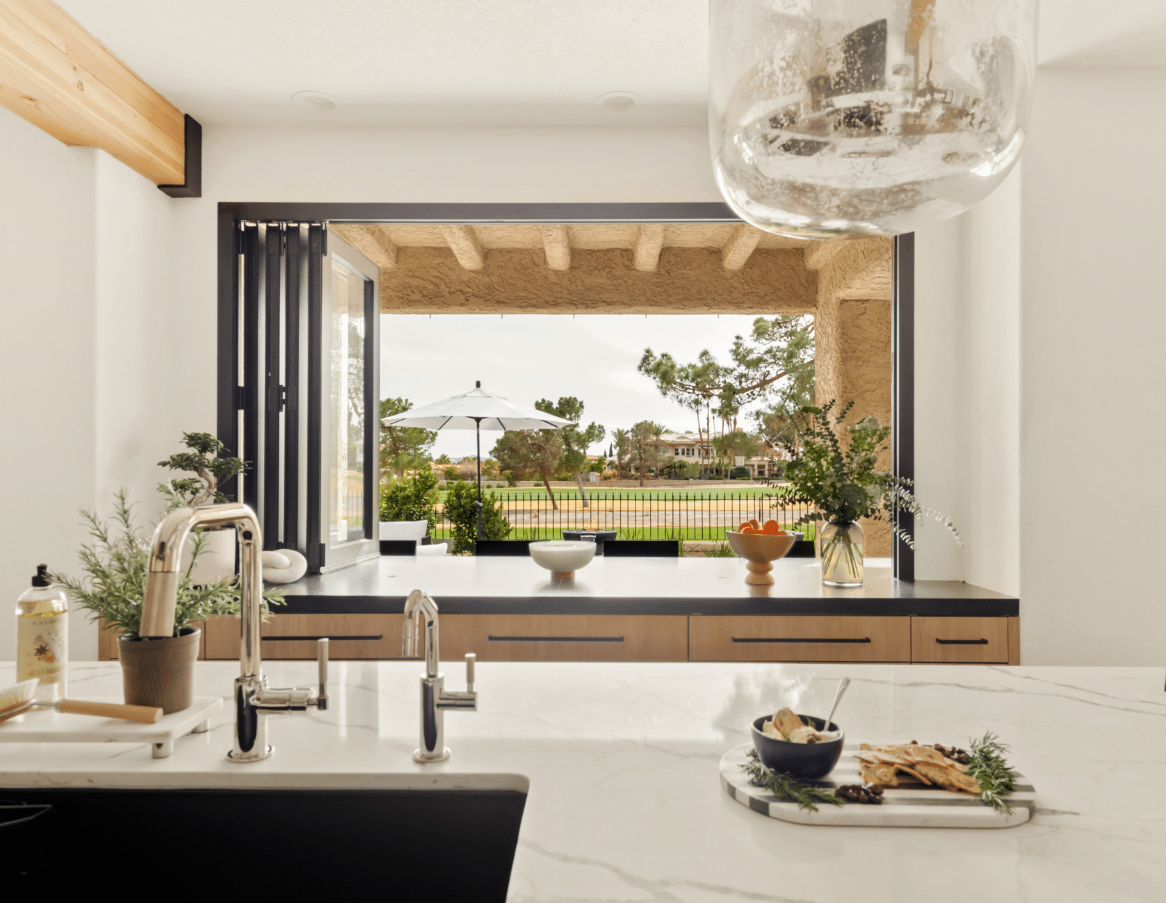 After: Marble waterfall island with black base, light wood cabinetry, and large black-framed window with golf course views in The Parker kitchen