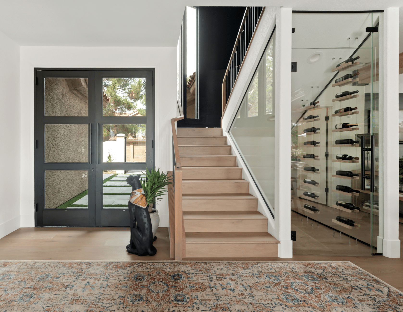 After: Light wood staircase with black metal railing, glass-enclosed wine display cabinet, and black-framed glass doors in The Parker