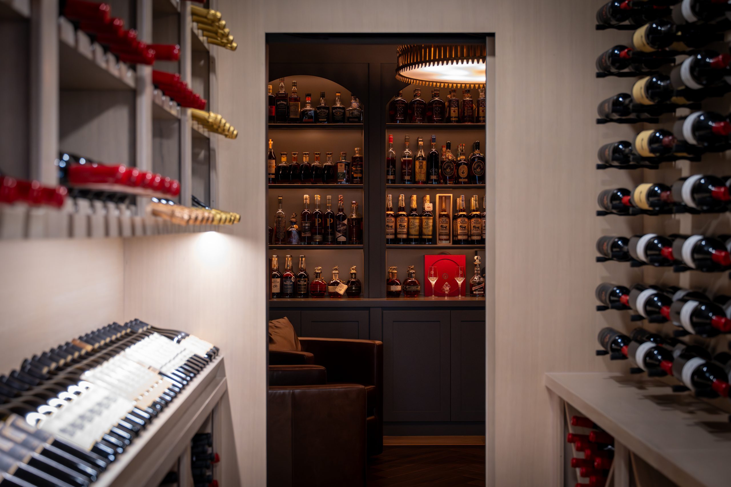 View from the wine cellar into the whiskey lounge, with custom oak wine racks framing the doorway and arched liquor displays visible beyond at The Charleston Southern Highlands remodel.