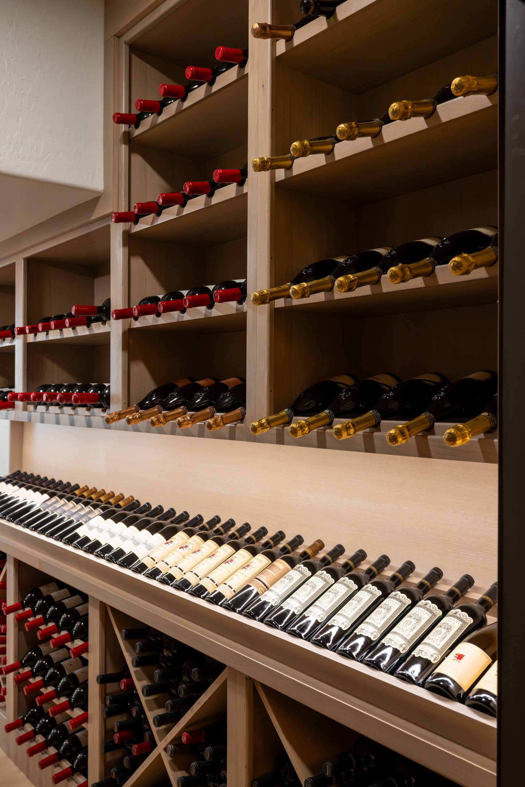 Custom white oak wine racking with diagonal and X-pattern storage holding red wines and Champagne at The Charleston Southern Highlands remodel wine cellar.