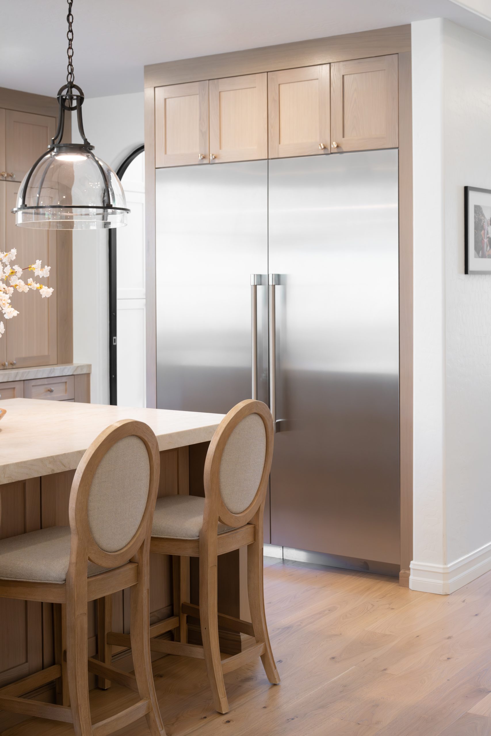 Built-in stainless steel French door refrigerator framed by white oak shaker cabinetry, with oval-back counter stools at the kitchen island, at The Charleston Southern Highlands remodel.
