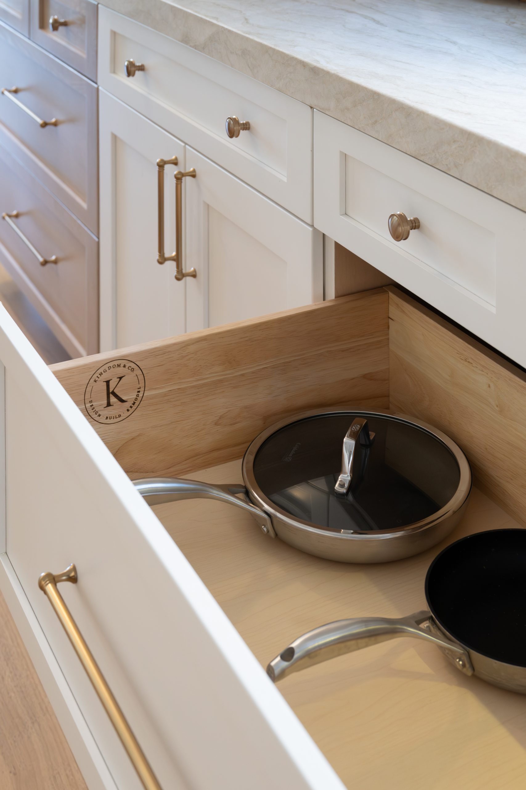 Open kitchen drawer detail with Kingdom & Co. branded cabinet interior, white shaker cabinetry, and brass cup pulls at The Charleston Southern Highlands remodel.
