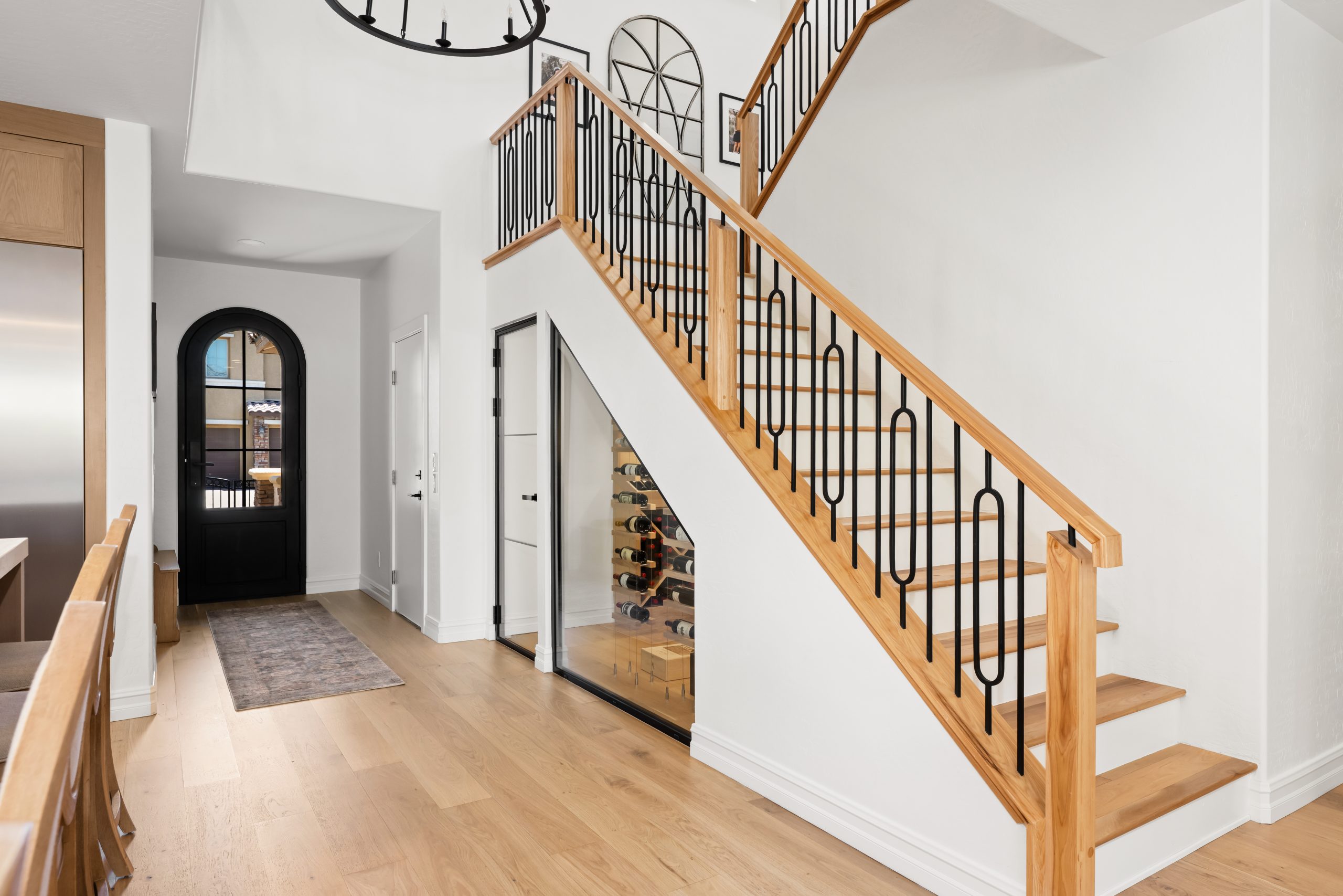 Two-story entry foyer with custom white oak staircase, geometric black wrought iron railing, under-stair glass-front wine cellar, and arched front door at The Charleston Southern Highlands remodel.