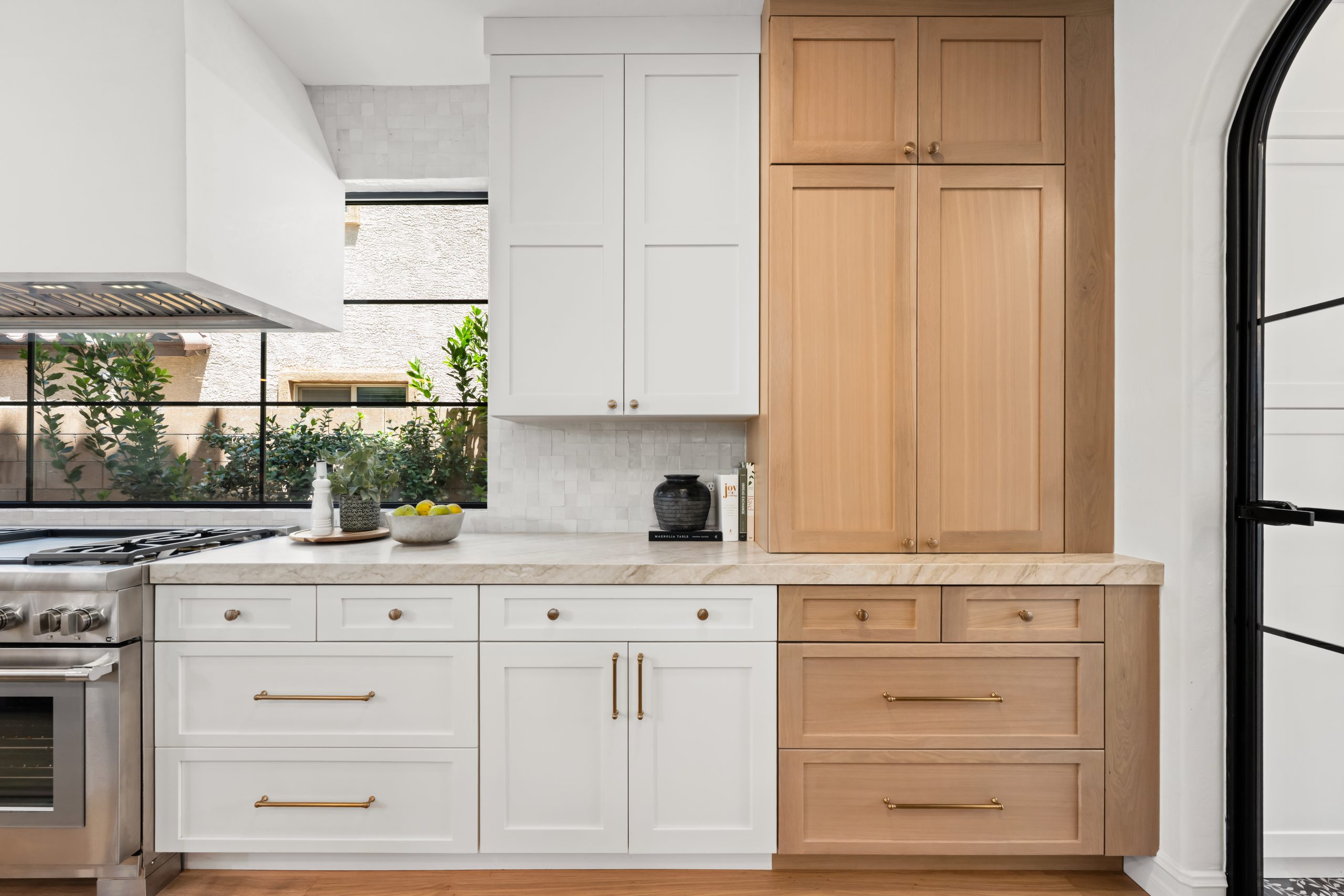 Two-tone kitchen elevation with white shaker cabinetry, a tall white oak pantry tower, white marble countertops, brass hardware, and zellige tile backsplash at The Charleston Southern Highlands remodel.