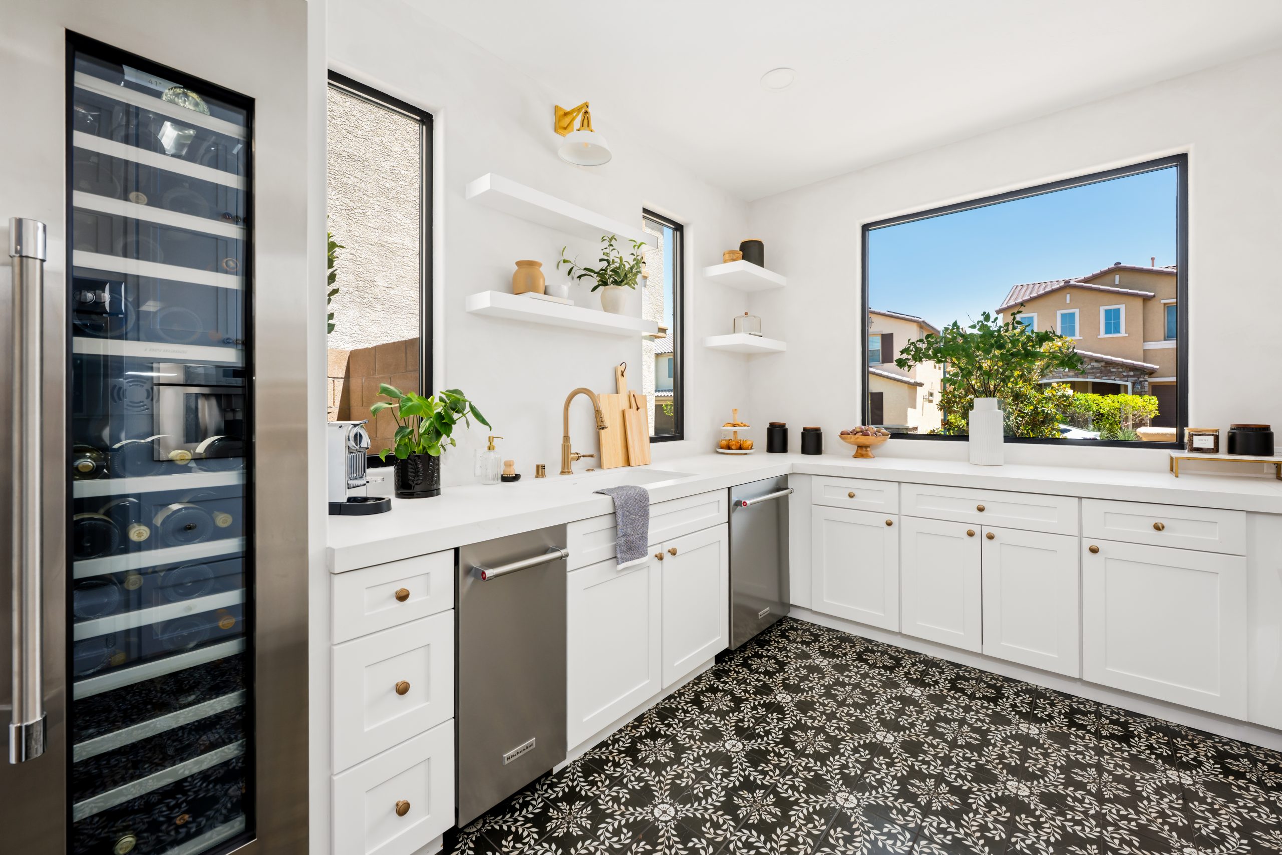 Scullery with large built-in glass-front wine refrigerator, prep sink, white shaker cabinetry, brass faucet, open shelves with greenery, and patterned floor tile at The Charleston Southern Highlands remodel.