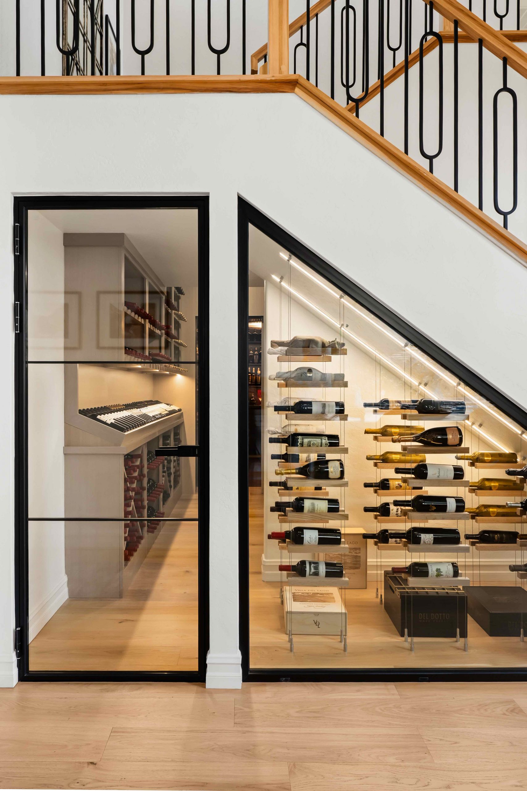 Custom under-stair wine cellar with black steel and glass enclosure, cable-suspended wine display rack system, and integrated LED lighting at The Charleston Southern Highlands remodel.