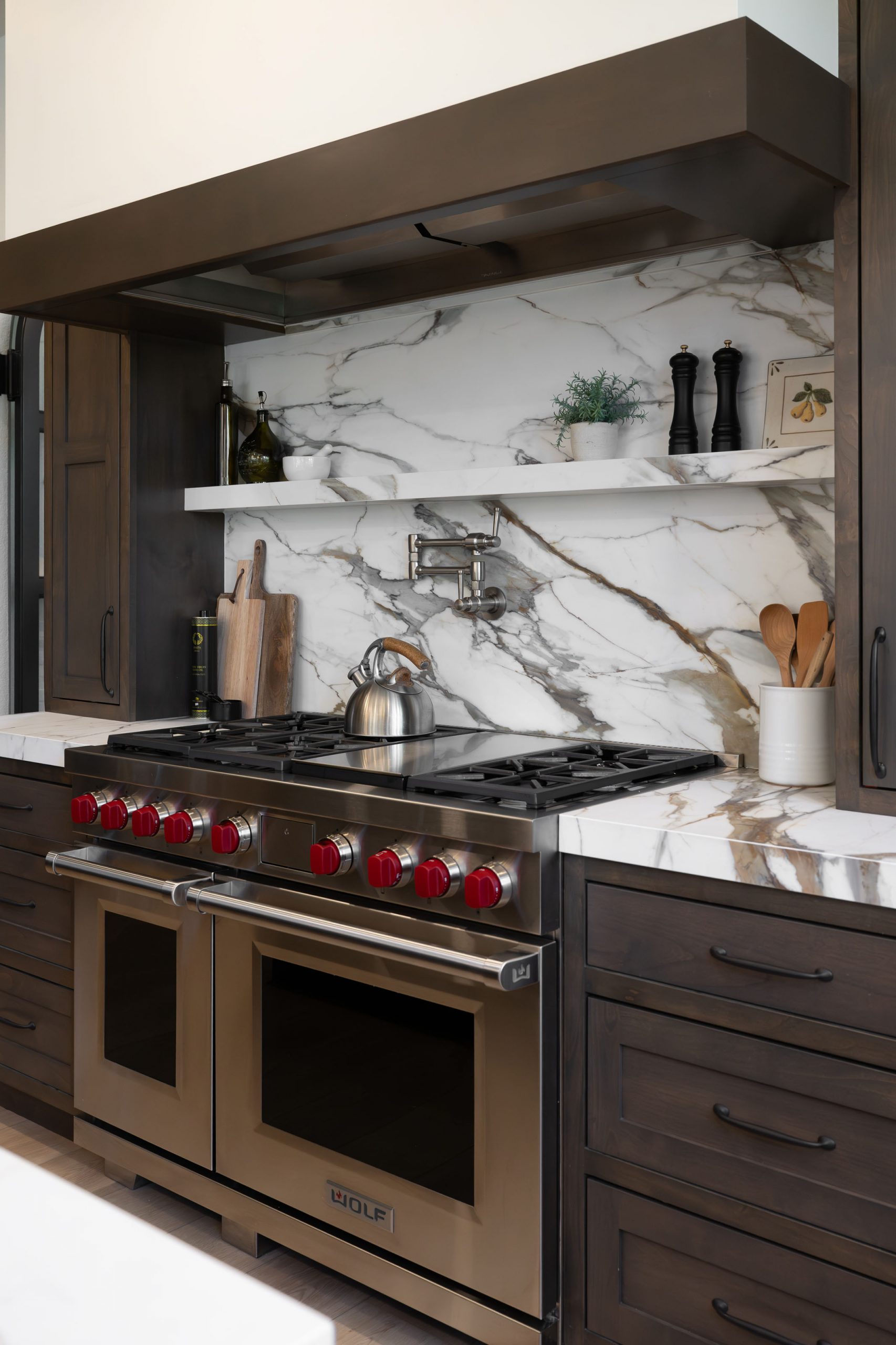Kitchen island with marble countertop, prep sink, bridge faucet, and two globe pendant lights in The Montecito Rhodes Ranch home remodel by Kingdom & Co.