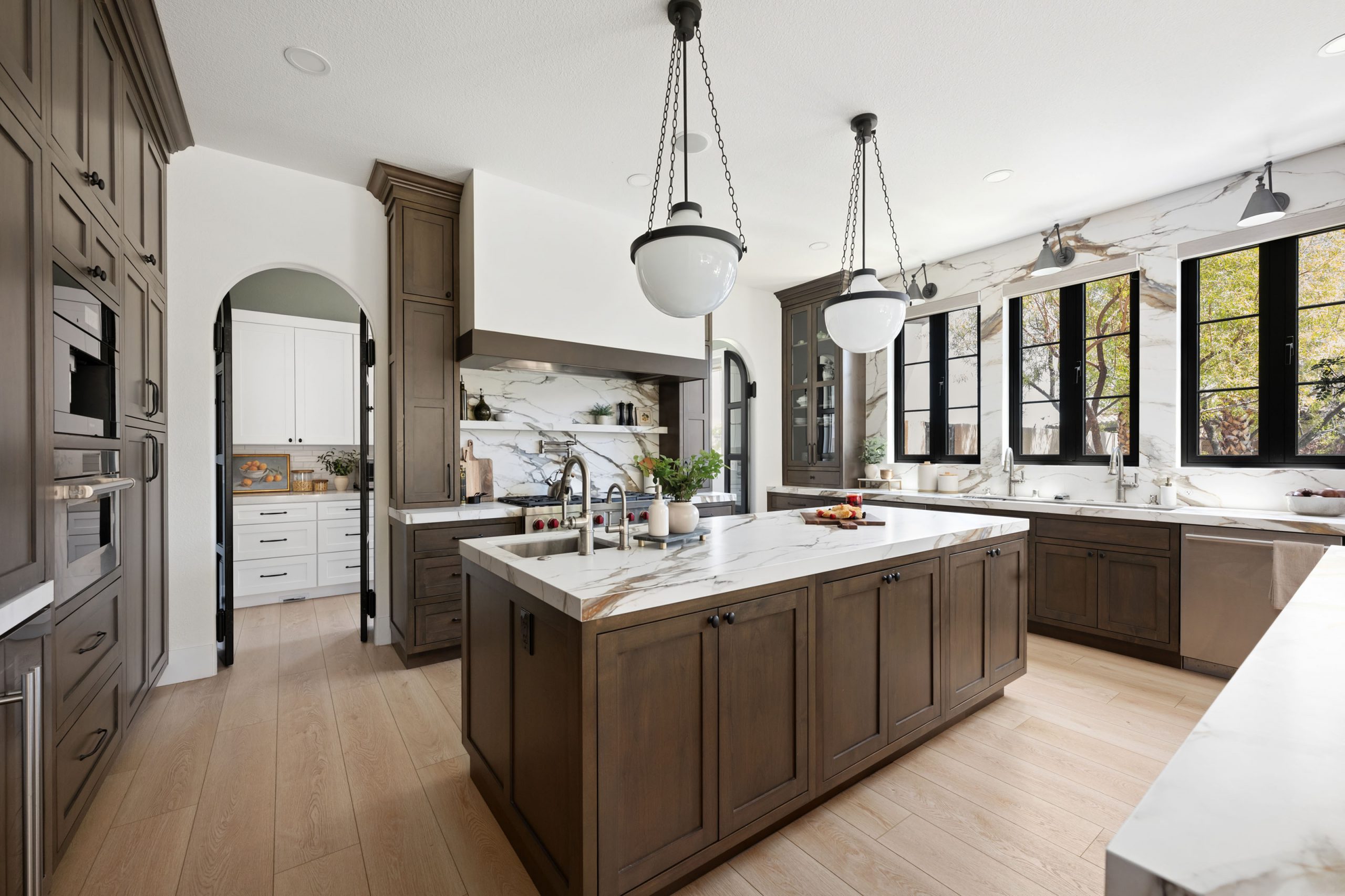 Remodeled kitchen with dark wood cabinetry, marble countertops, and arched pantry doorway in The Montecito home remodel by Kingdom & Co. in Rhodes Ranch