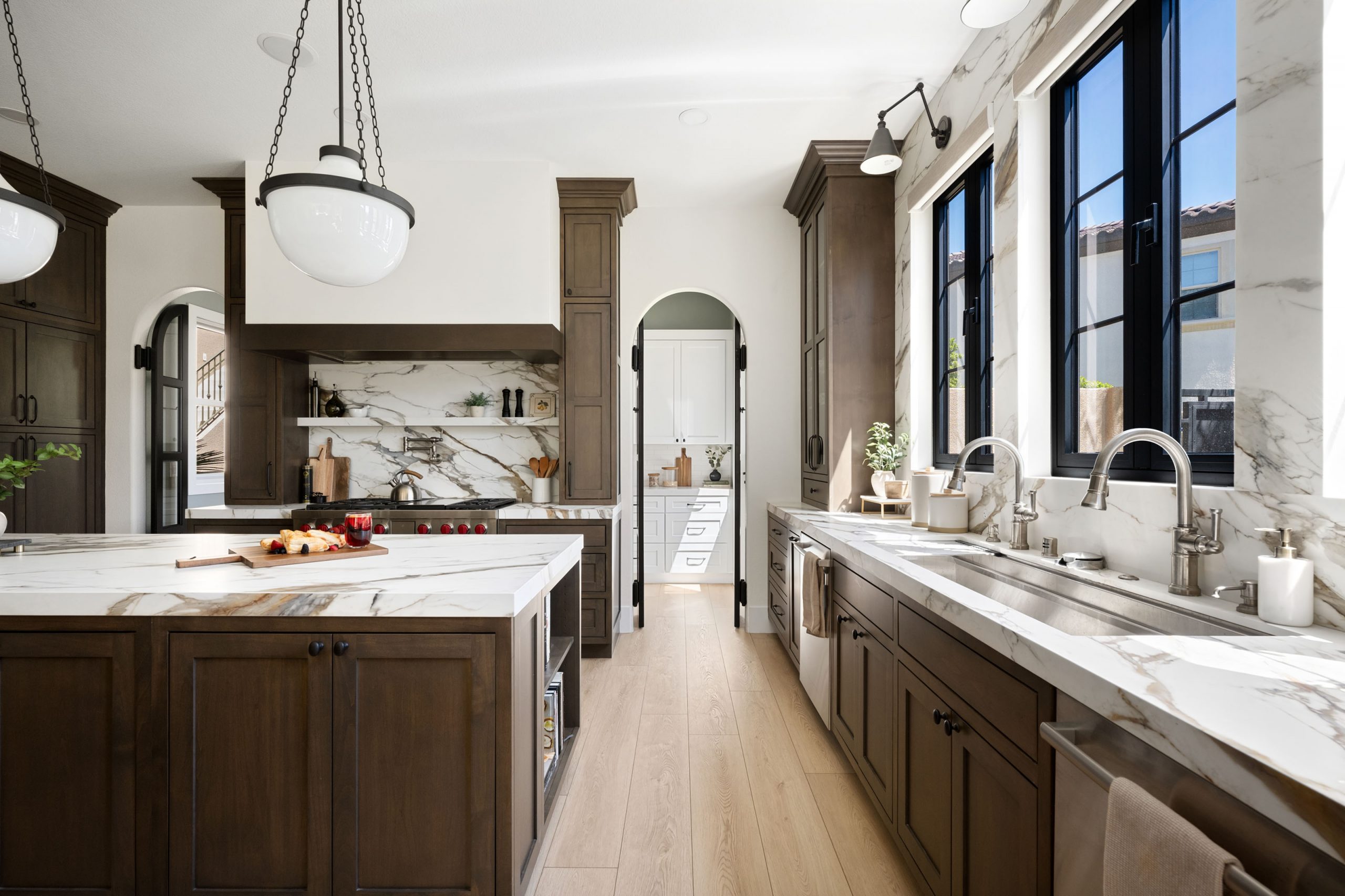 The Montecito – Kitchen Remodeled kitchen with Wolf range, marble slab backsplash, arched steel-and-glass pantry doorway, and dark wood cabinetry in The Montecito Rhodes Ranch home remodel by Kingdom & Co.
