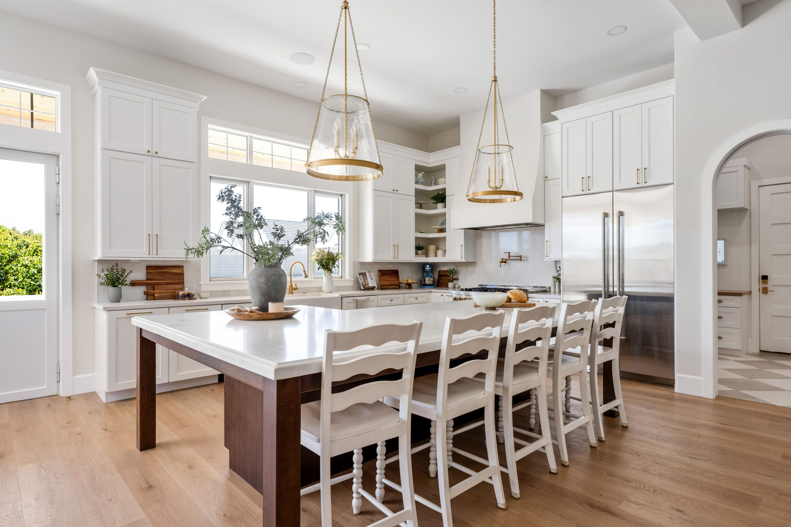 White Gables Estate007 Custom kitchen with stained wood island, white shaker cabinetry, brass pendant lanterns, mixed-metal hardware, and turned-leg counter stools — The White Gables Estate cottage style custom home Las Vegas by Kingdom & Co.