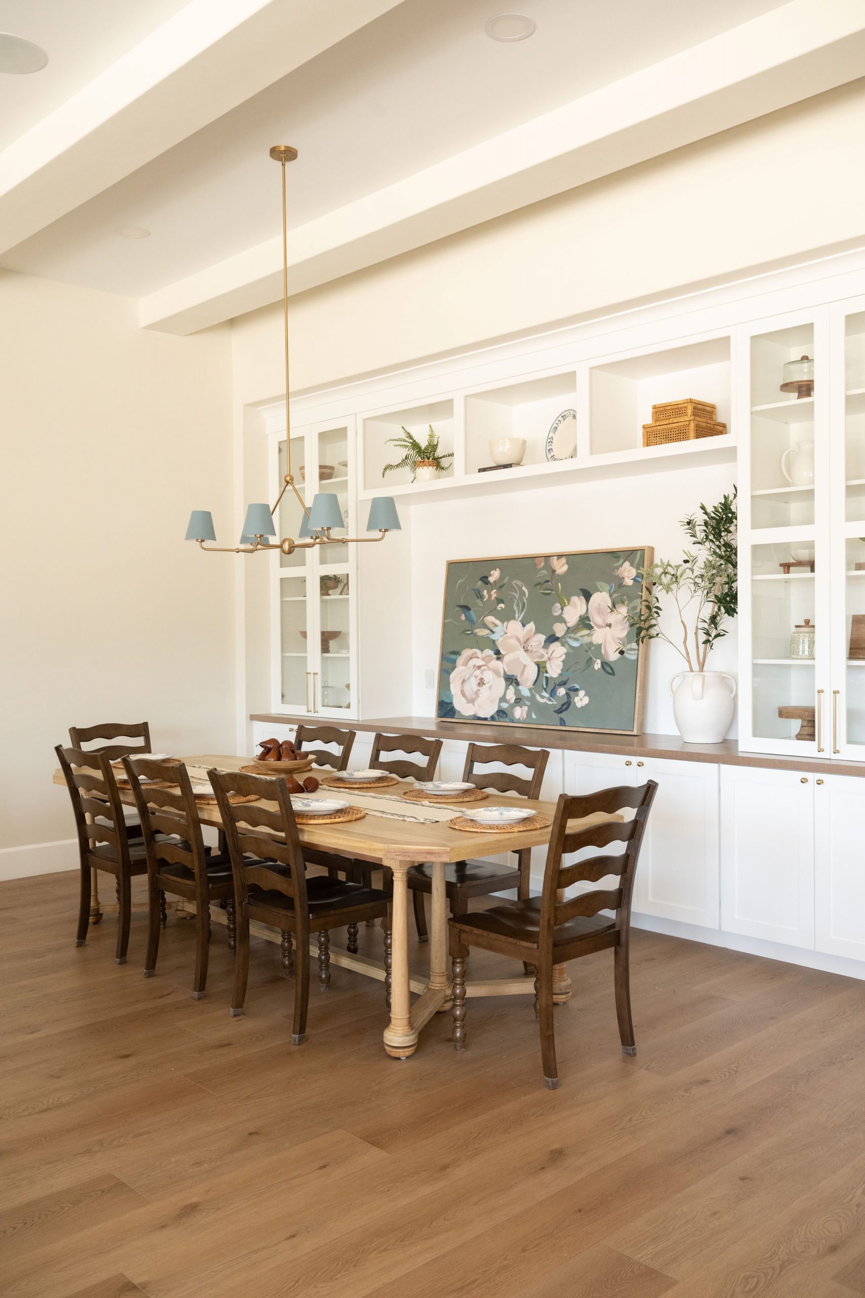 Cottage style dining room with built-in glass-front china cabinet, blue-shaded brass chandelier, wood dining table, and ladderback chairs — The White Gables Estate by Kingdom & Co.