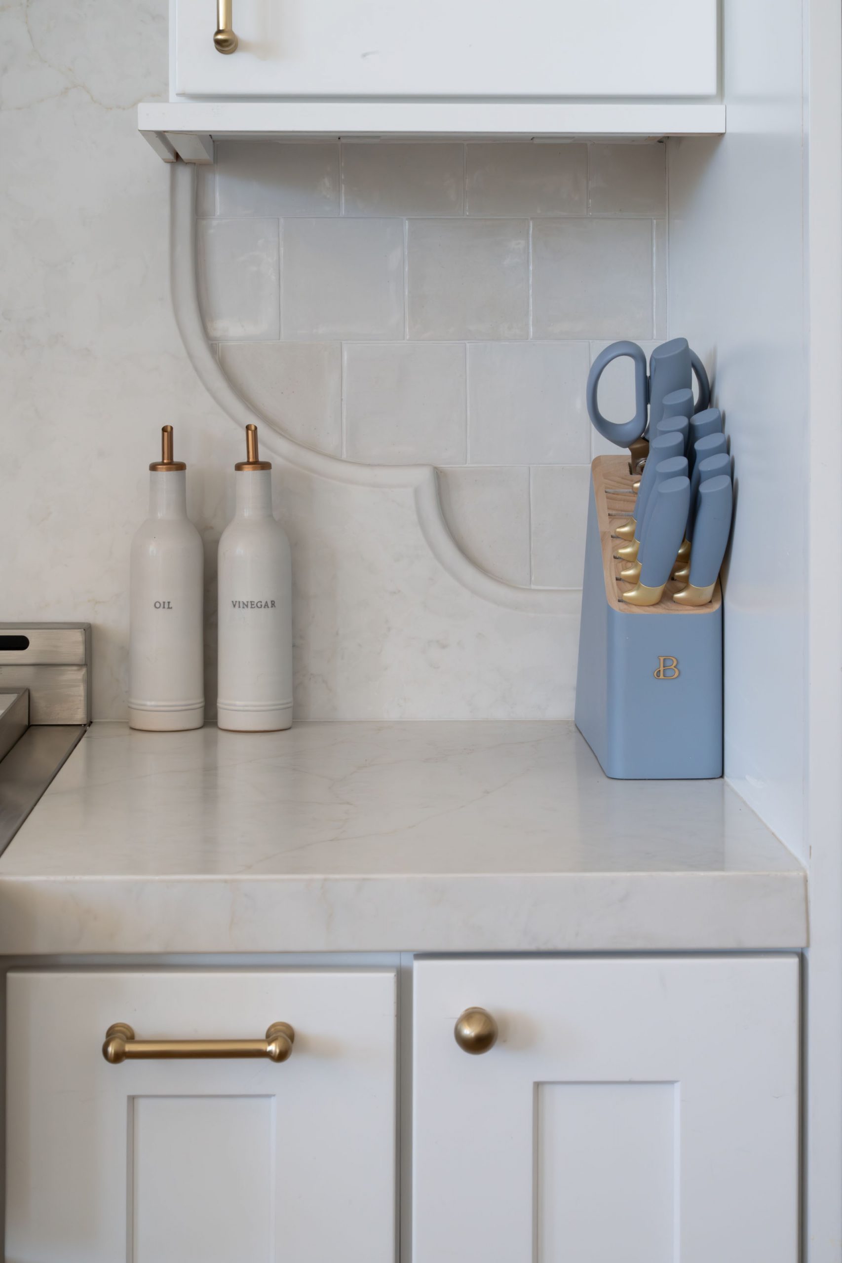 Kitchen detail with brass pot filler, handmade-look subway tile backsplash, stone countertop, and brass cabinet hardware — The White Gables Estate by Kingdom & Co