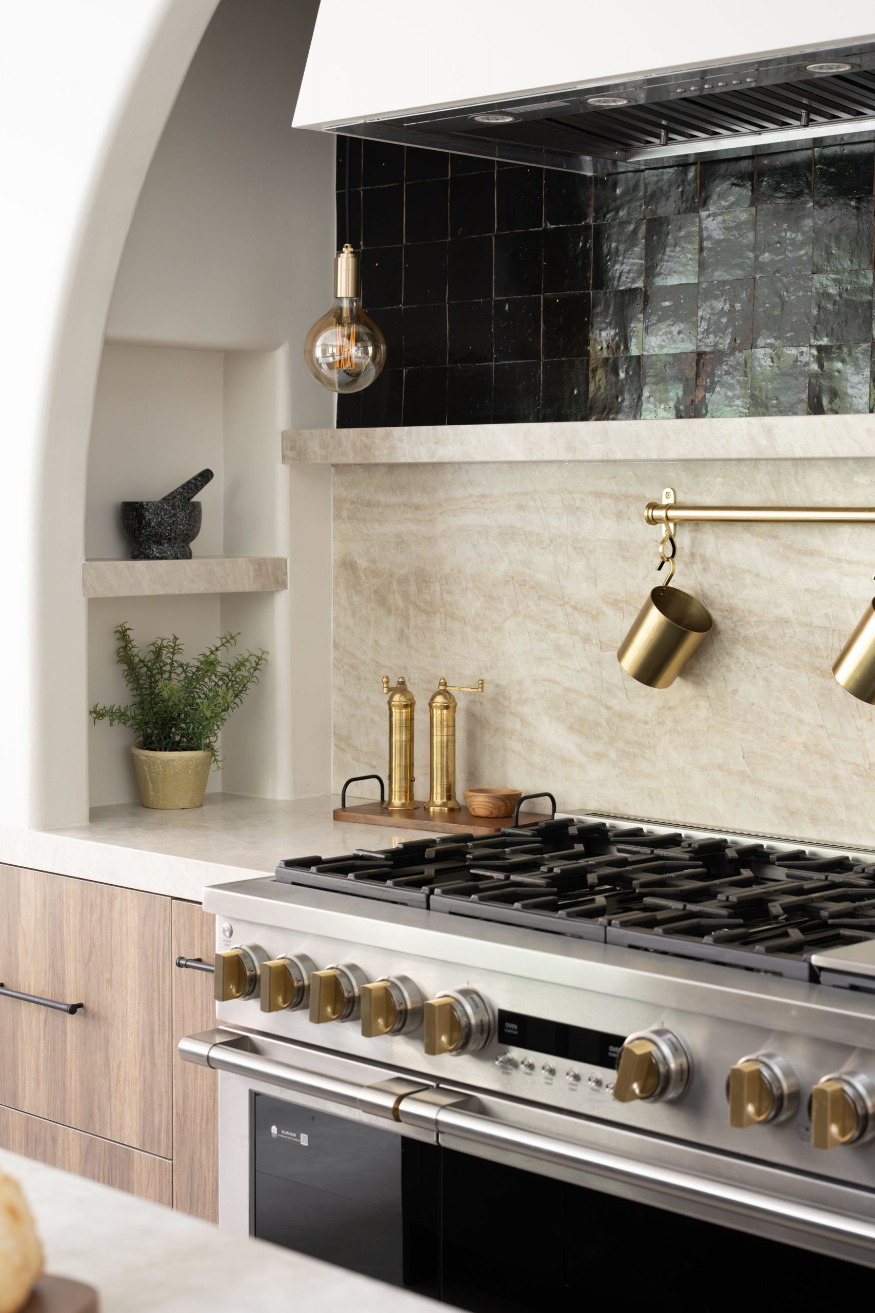 The Devonshire_19 Summerlin kitchen remodel by K&Co., arched plaster range alcove with black zellige tile, a stone slab backsplash and a brass pot rail
