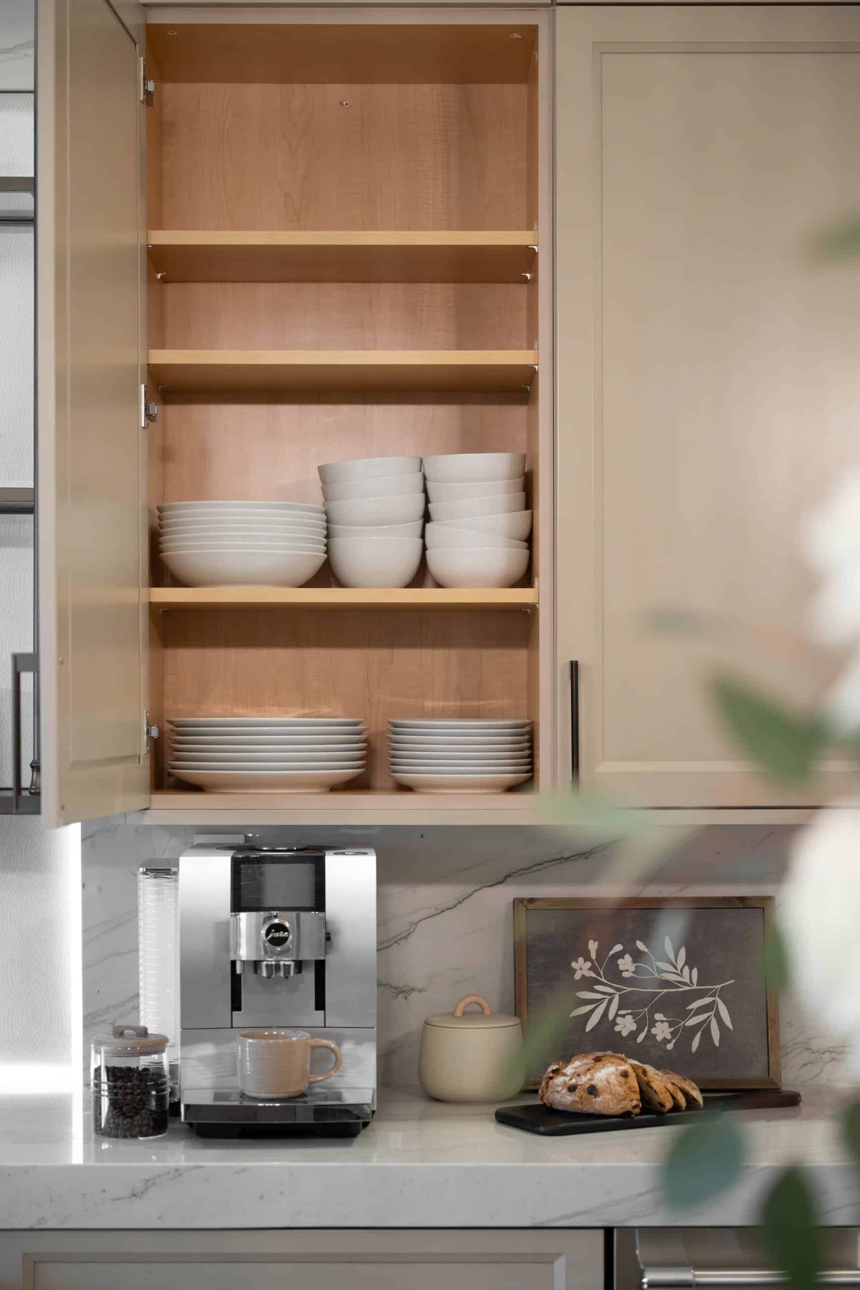 The Volere_33 Built-in Jura espresso coffee bar detail at The Volere in Silverado Ranch, Henderson, with open cabinet display of white ceramic dishware and calacatta marble countertop, part of the Kingdom & Co. Small Luxuries kitchen remodel.