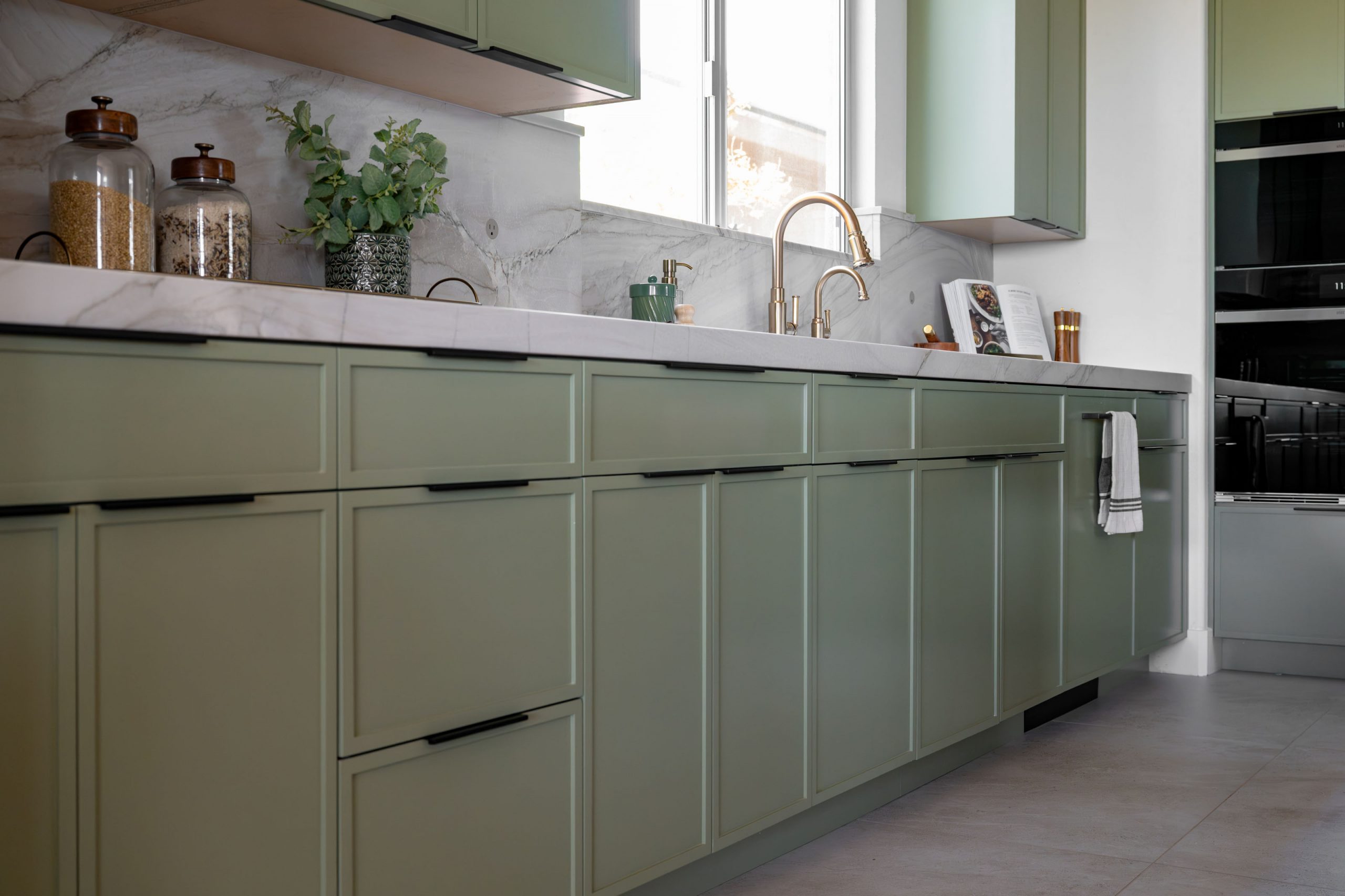 Sage green base cabinets, brass faucet, and marble waterfall backsplash, Kingdom & Co. Summerlin kitchen.