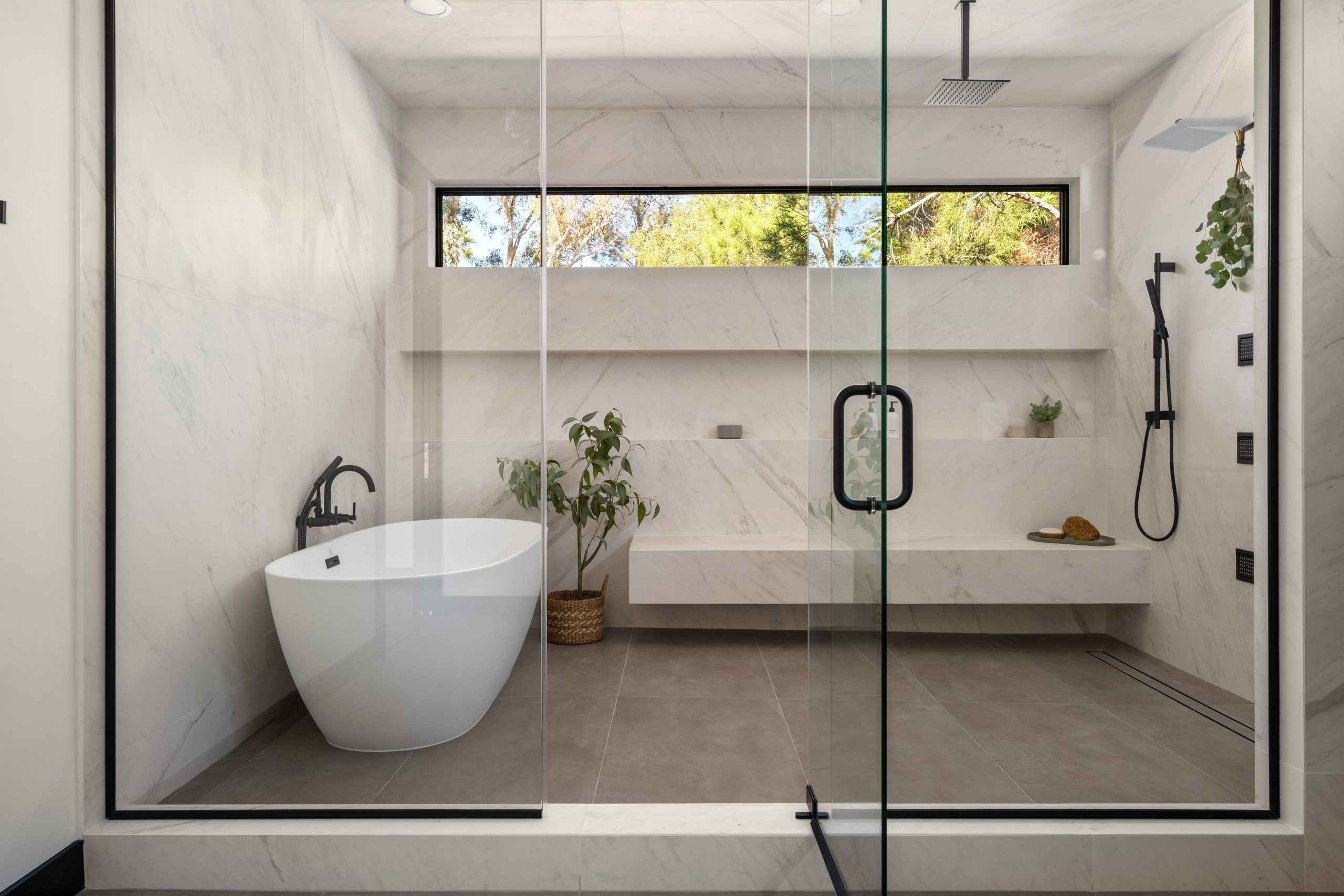 The Brixton_TheLakes_WholeHomeRemodel11 Primary spa wet room with freestanding tub, marble bench, and rain shower behind black steel glass, Kingdom & Co. The Lakes.