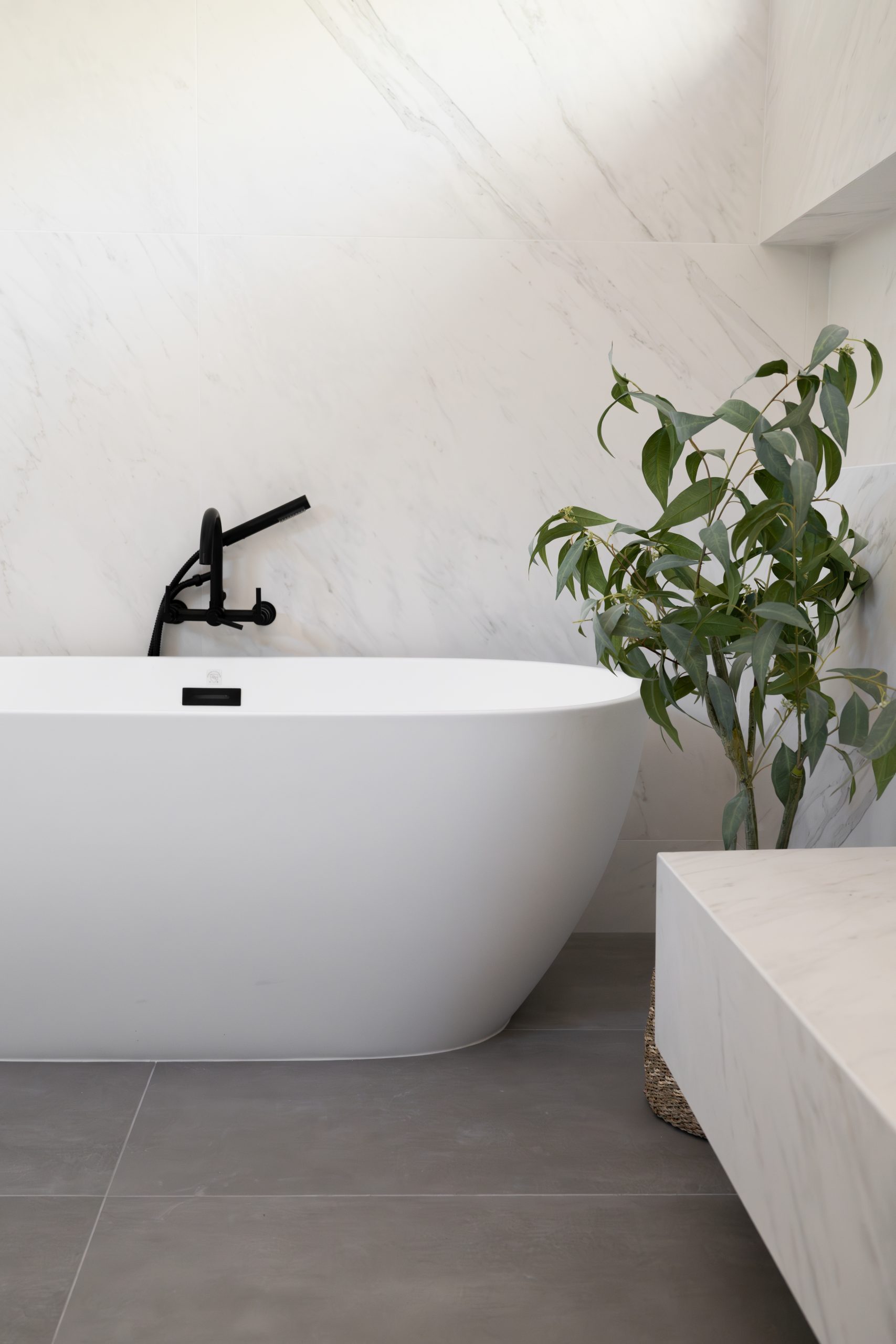 Freestanding tub with black wall-mount tub filler against marble slab wall, Kingdom & Co. The Lakes primary spa.