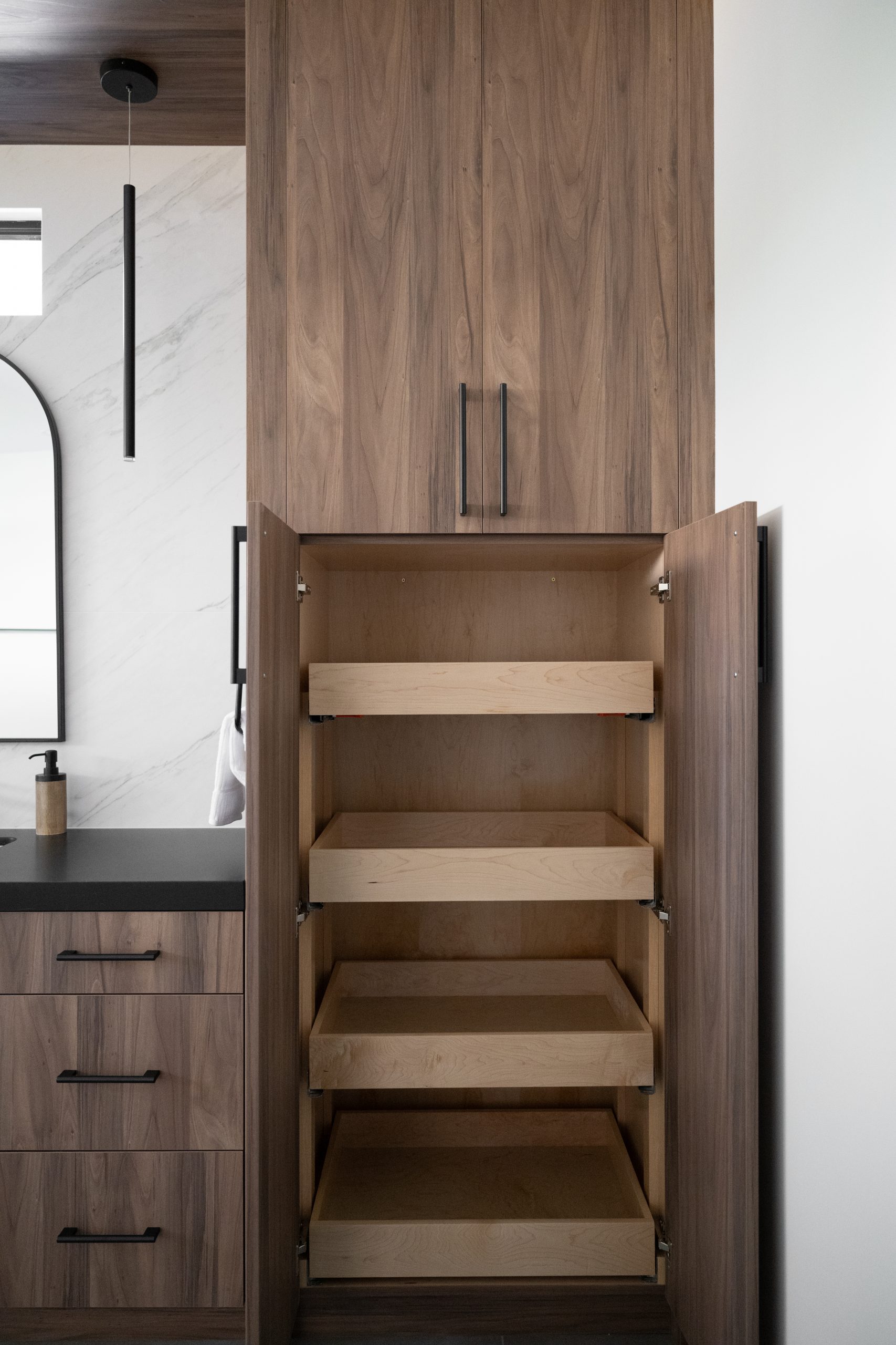 Walnut floor-to-ceiling linen tower with maple pull-out shelves in primary bath, Kingdom & Co. The Lakes remodel.
