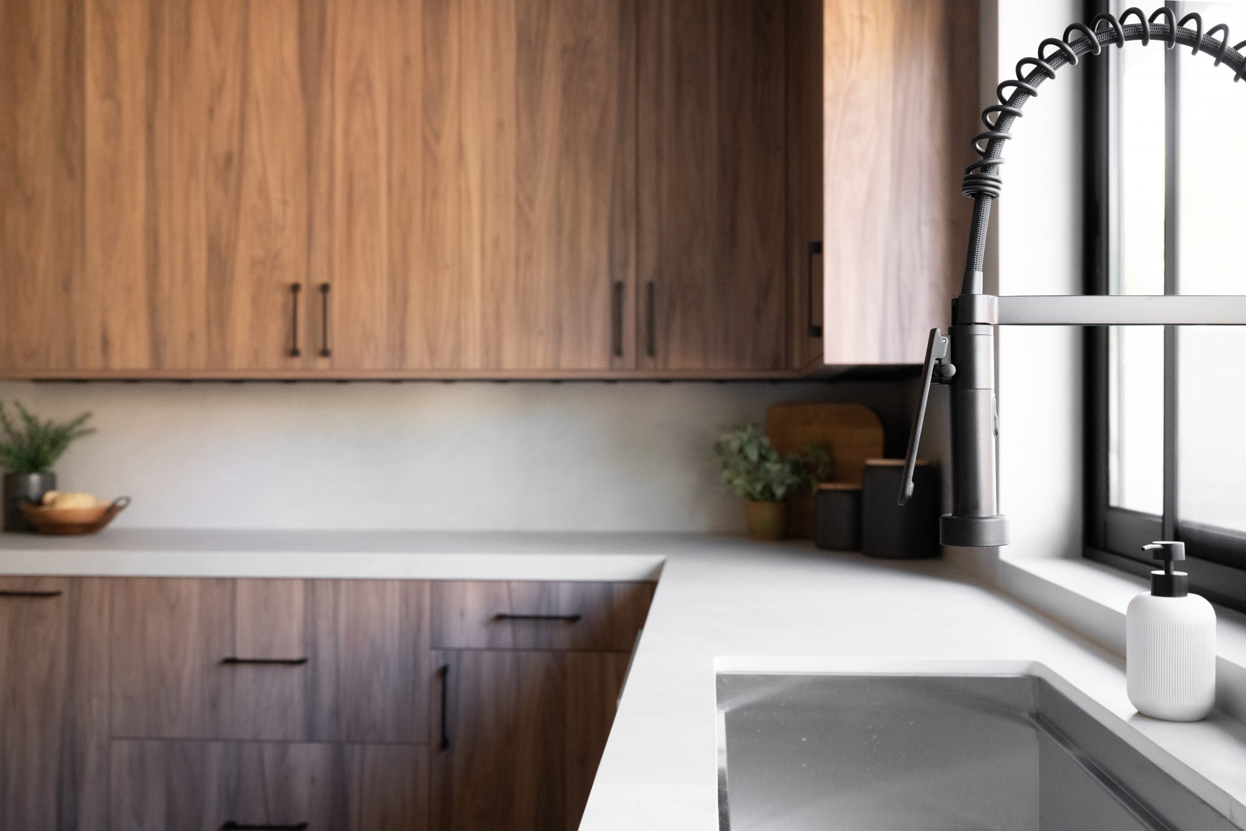 Walnut kitchen sink detail with black spring faucet at black steel window, Kingdom & Co. The Lakes remodel.