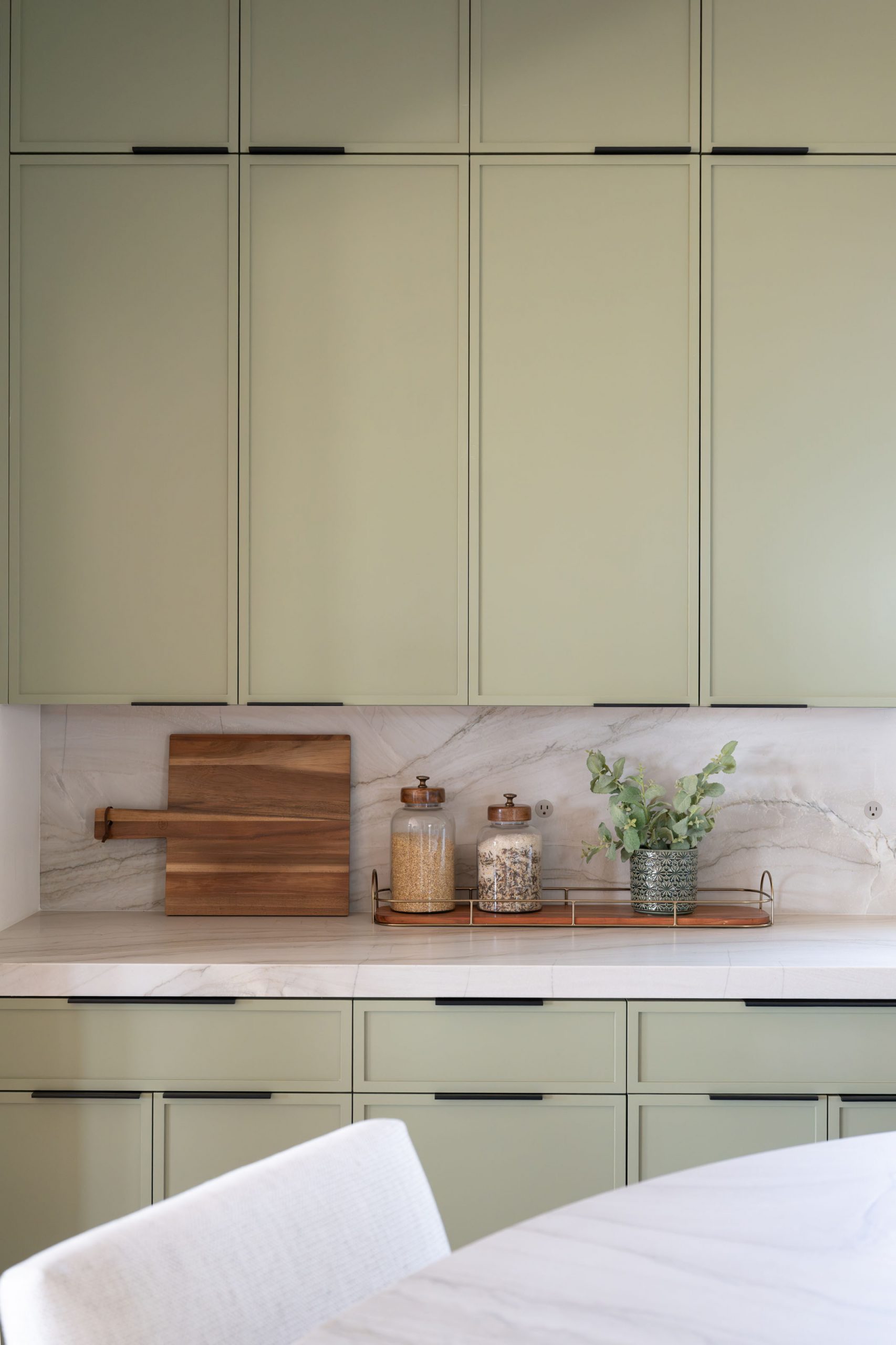 Sage green cabinets and marble backsplash detail with cutting board and canister styling, Kingdom & C