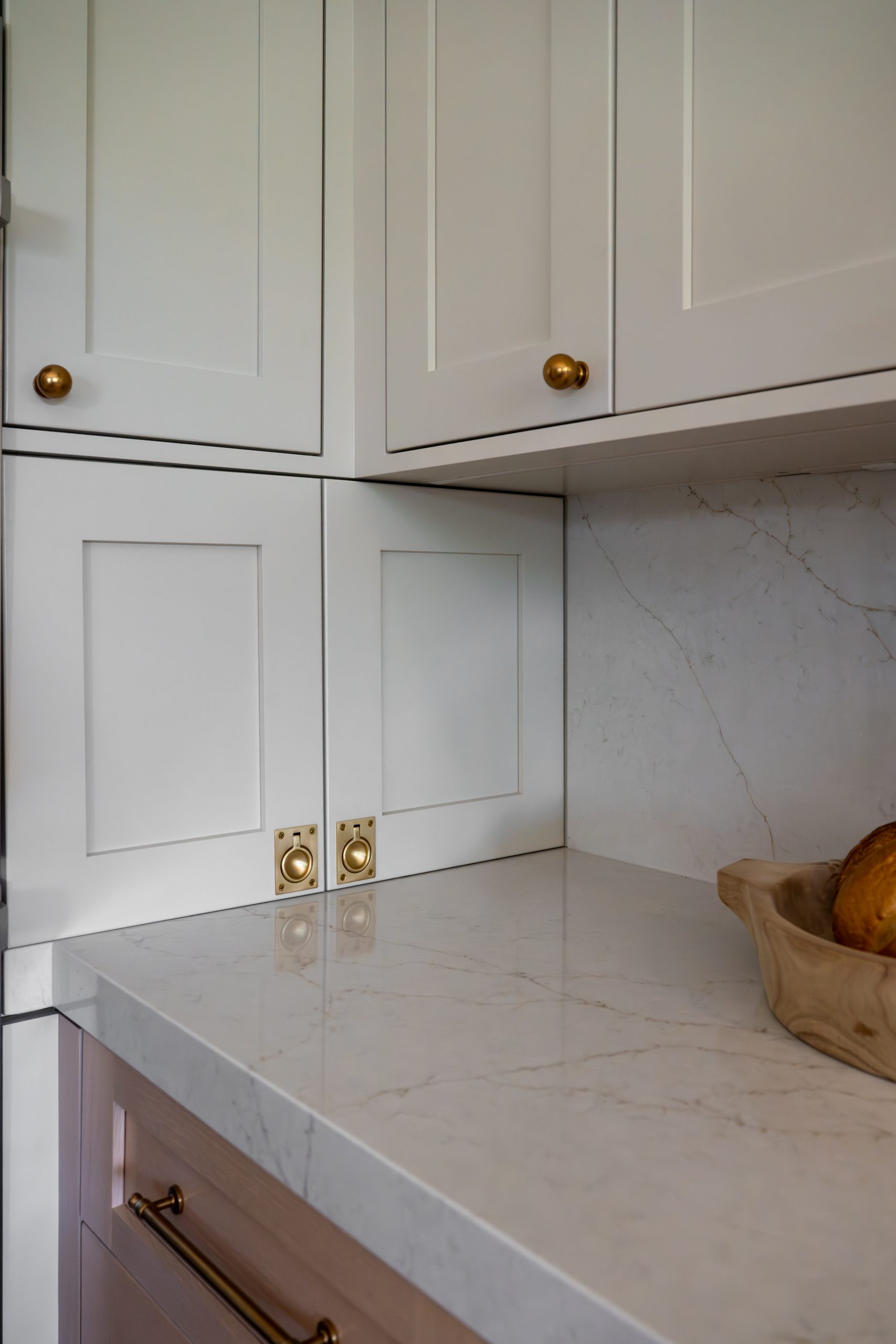 Custom appliance garage with brass ring pulls beside sourdough loaves, Kingdom & Co. The Hearthstone kitchen.