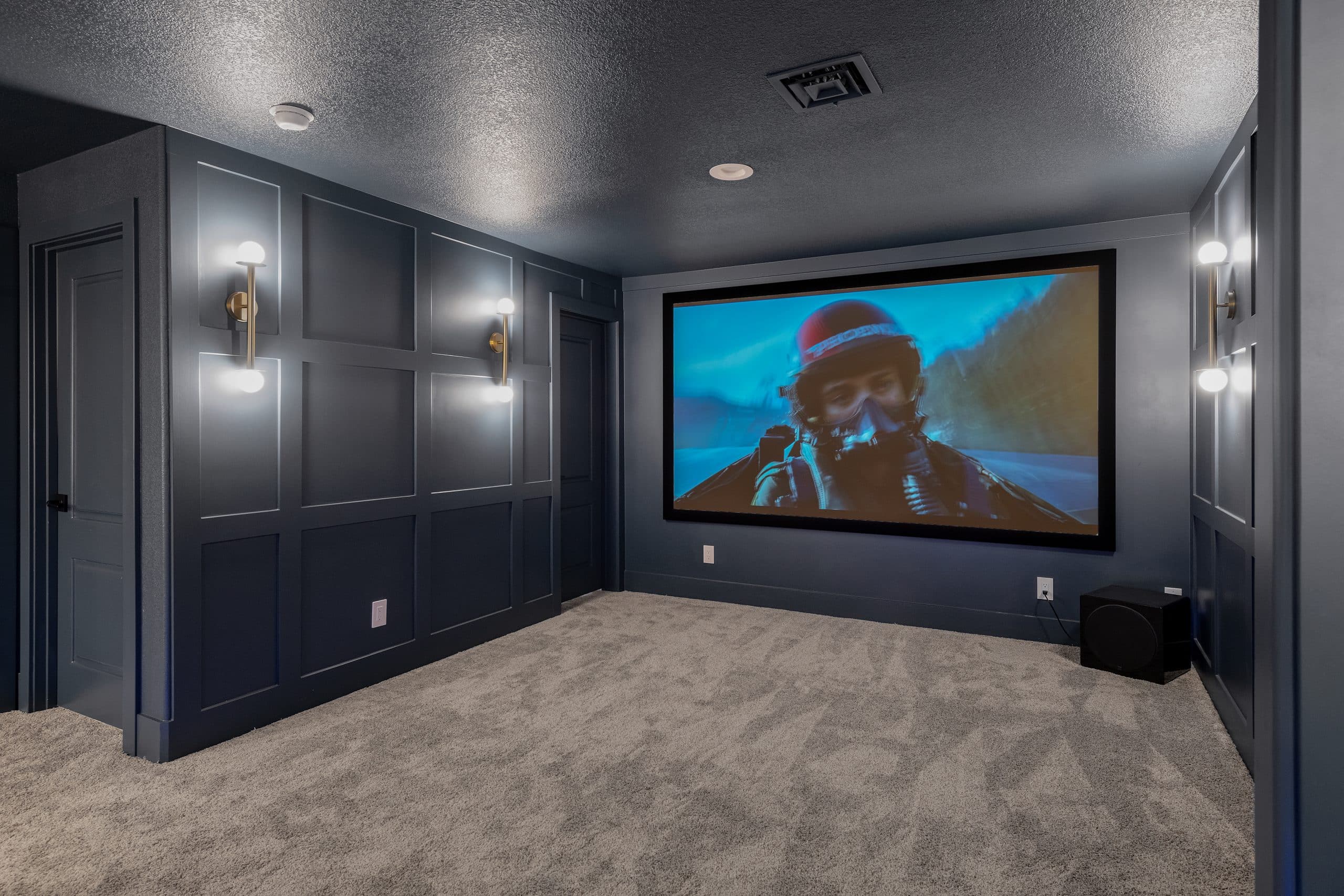 Basement movie theater in Willows Summerlin home renovation by Kingdom & Co. — navy paneled walls, projection screen, brass sconces