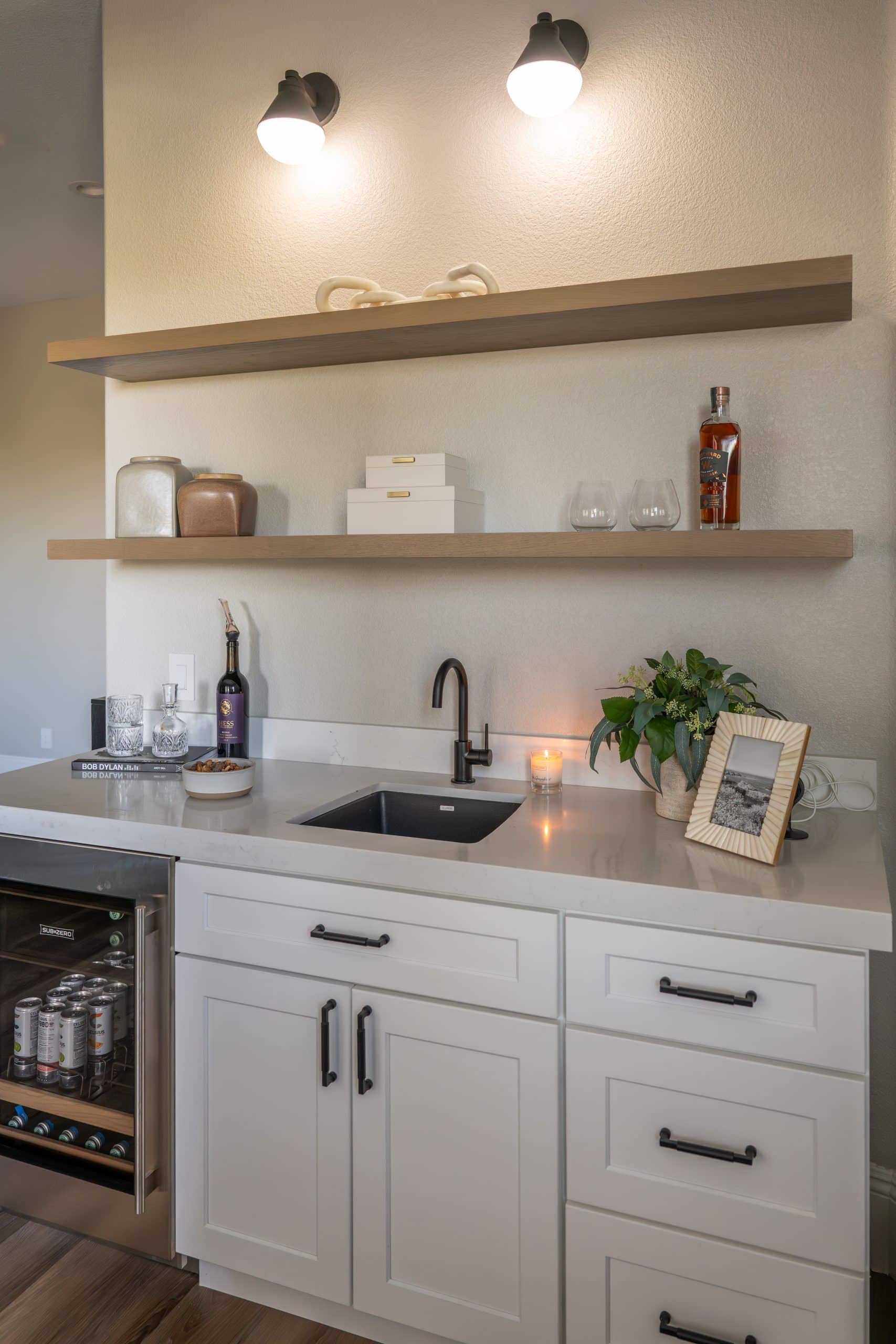 The_Ashford60 Primary suite beverage bar in Willows Summerlin home renovation by Kingdom & Co. — white shaker cabinets, matte black hardware, Sub-Zero fridge