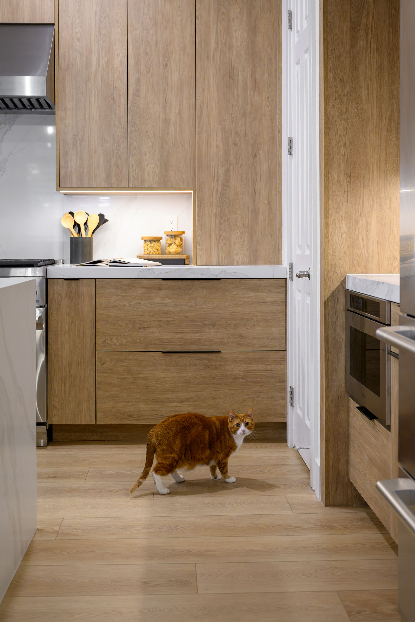 Kitchen vignette with warm oak cabinetry, lit under-cabinet niche, and built-in stainless wall oven in Summerlin remodel by Kingdom & Co.