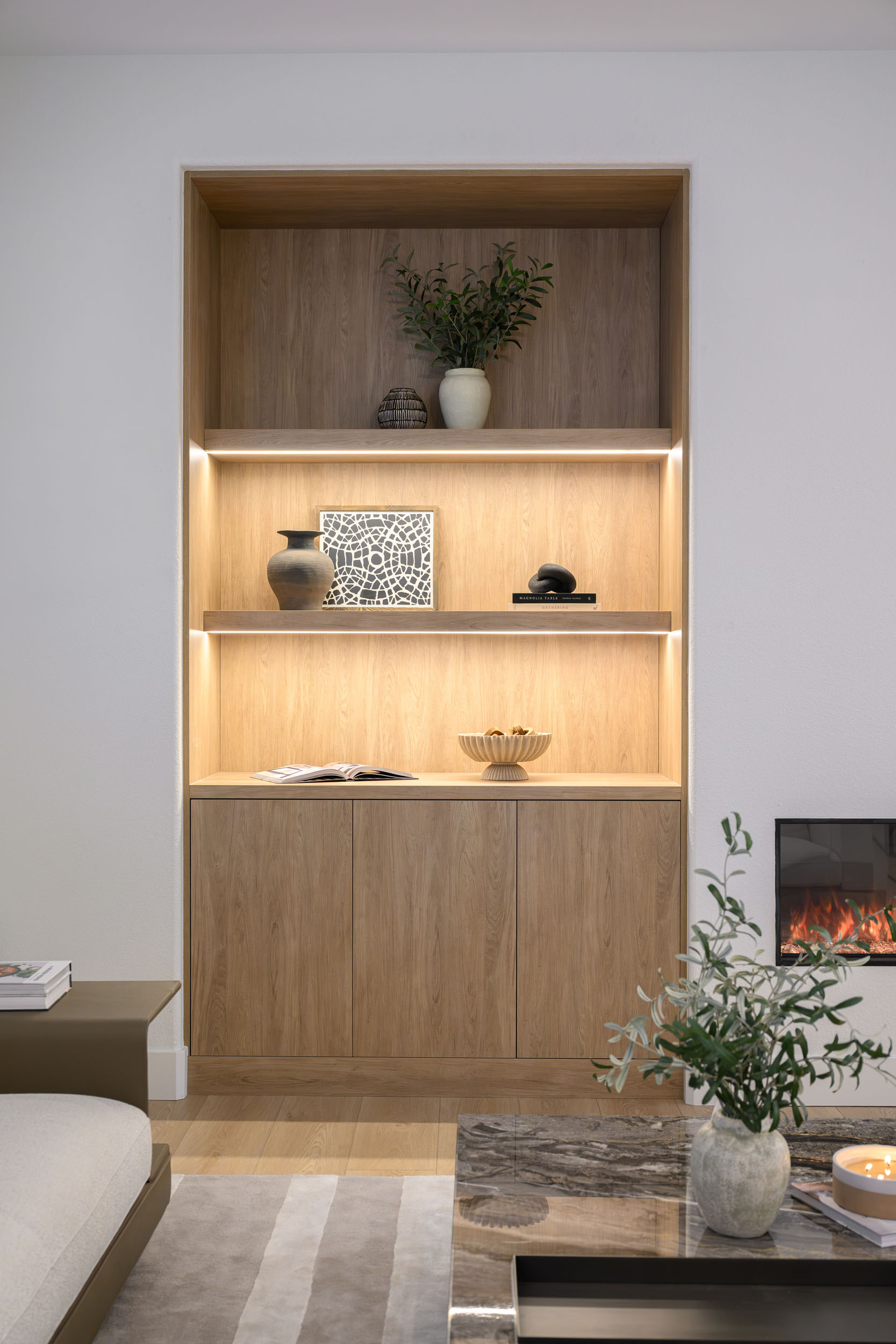 The_Elysian_SummerlinRemodel_Kingdom30 Living room warm-oak built-in bookcase and linear gas fireplace with bouclé sofa and round marble coffee table in Summerlin remodel by Kingdom & Co.