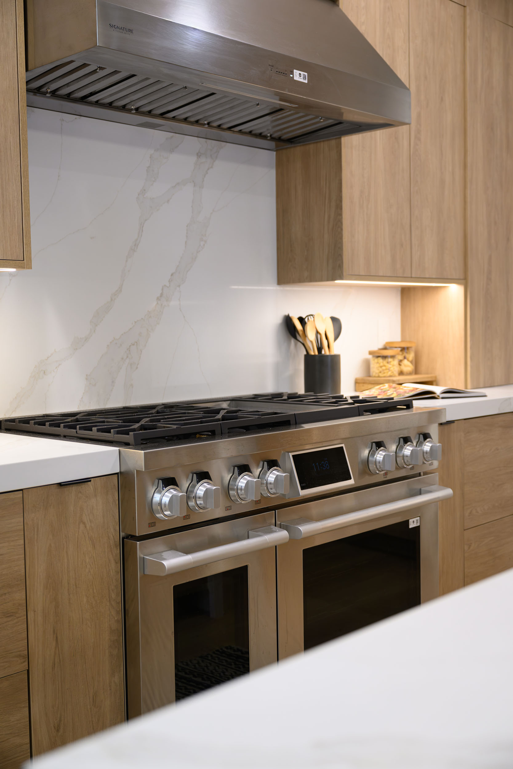 Stainless gas range detail under integrated hood framed by warm oak cabinetry and full-height marble slab backsplash in Summerlin remodel by Kingdom & Co.