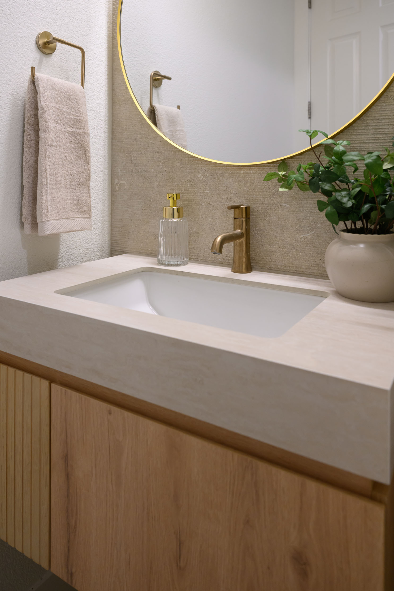 Powder room detail of integrated stone sink and brass single-handle faucet on fluted oak floating vanity in Summerlin remodel by Kingdom & Co.