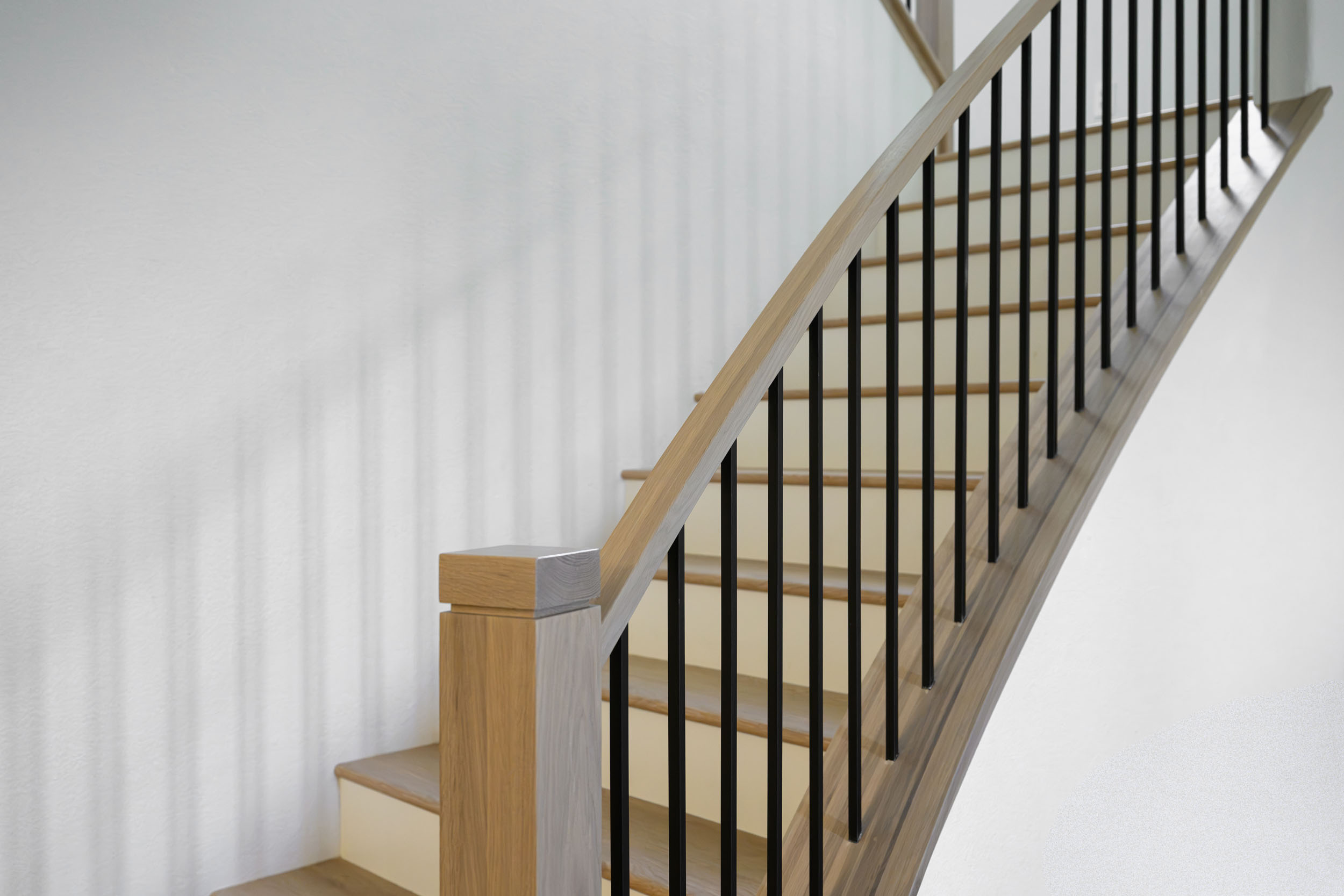 Curved light oak staircase handrail with slim black metal spindles and painted risers in Summerlin remodel by Kingdom & Co.